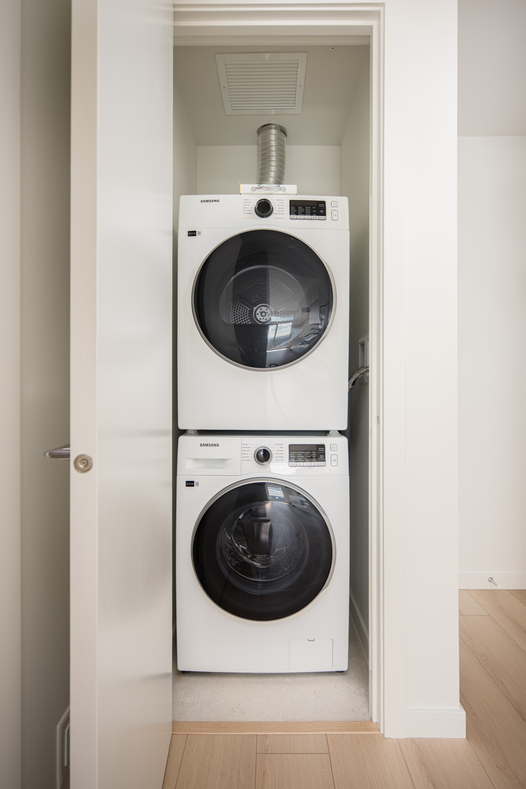 A stacked washer and dryer set is installed in a narrow laundry closet with the door open, revealing both front-loading machines.