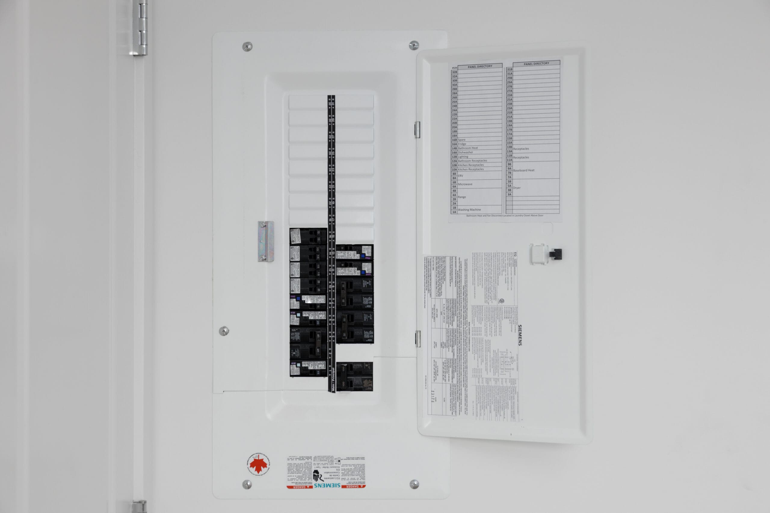 An open electrical breaker panel with labeled circuits, mounted on a white wall.