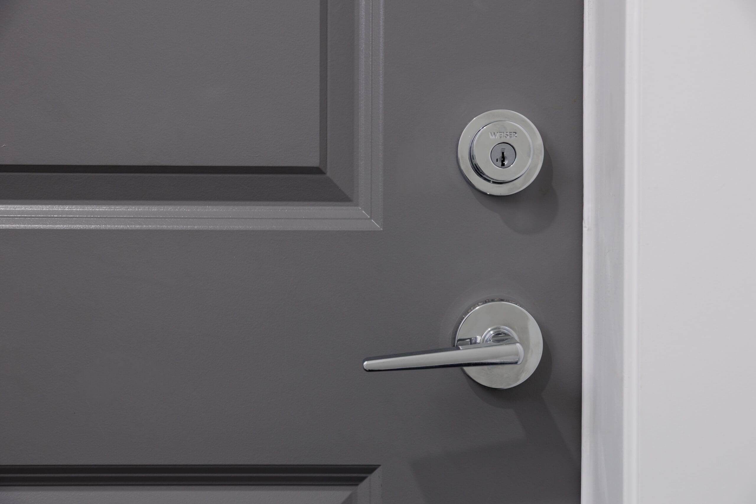 Gray door with a round deadbolt lock and a silver lever handle, shown from a close-up perspective.