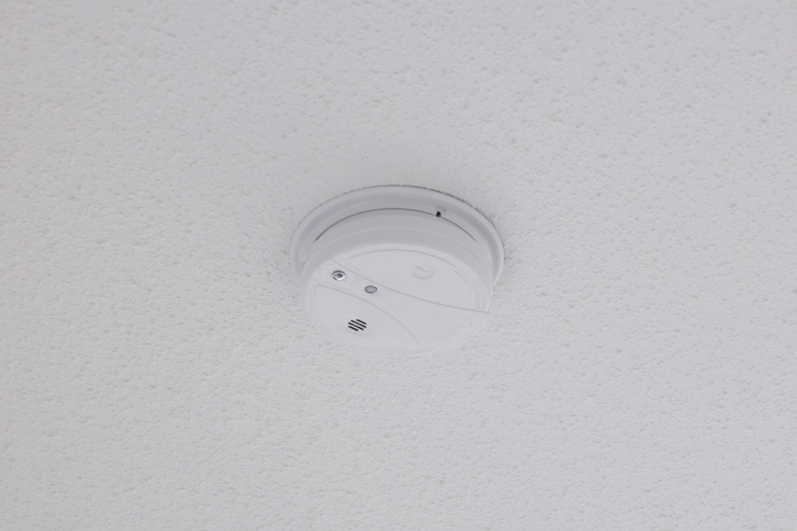 A smoke detector mounted on a white, textured ceiling.
