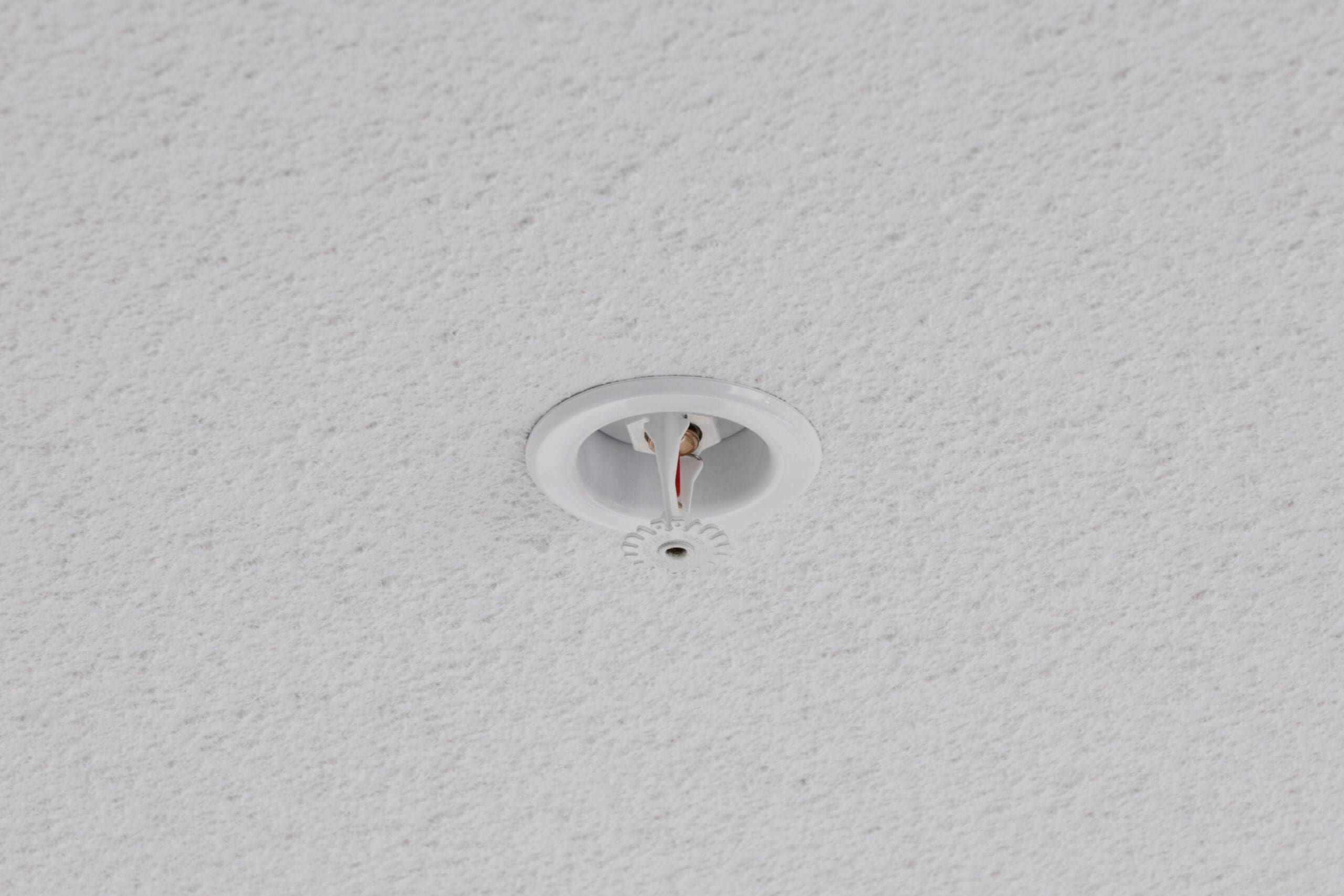 A round ceiling sprinkler head with exposed wires is installed in a textured white ceiling.