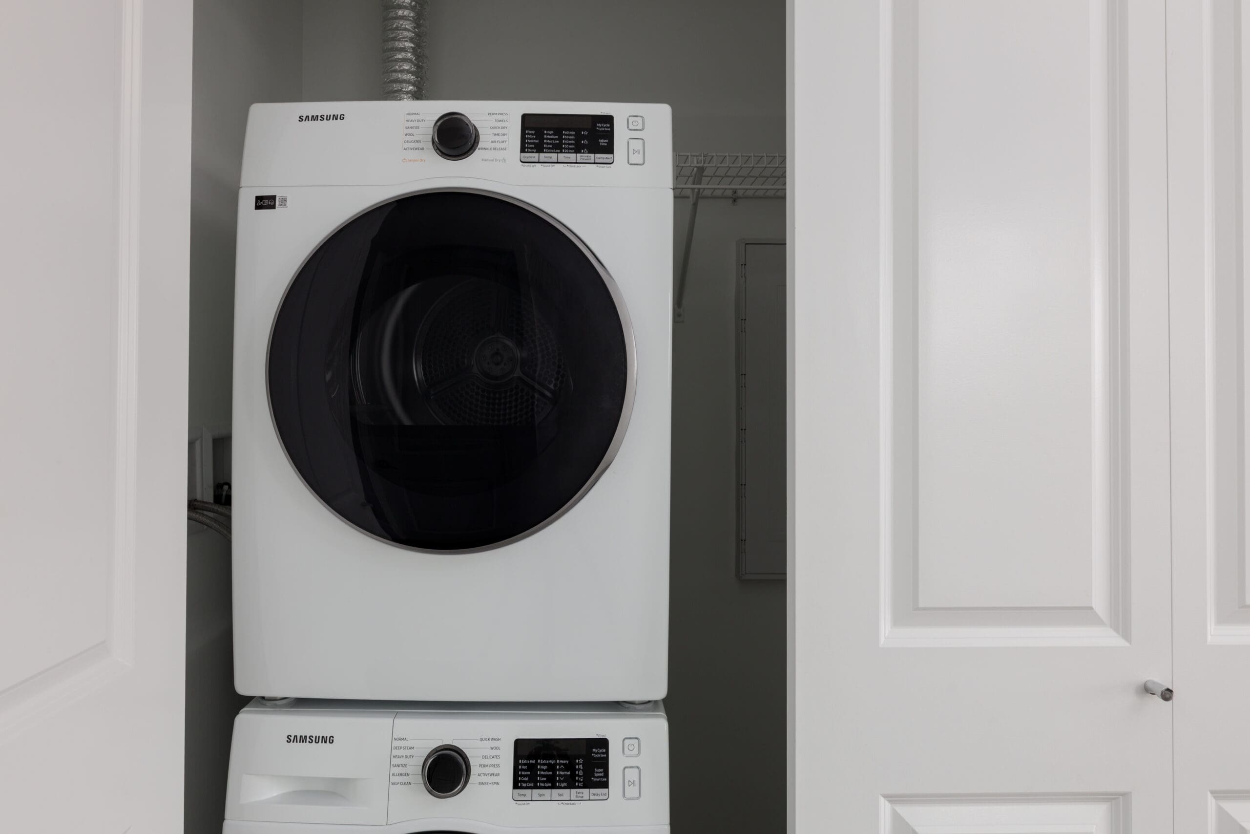 Stacked front-loading Samsung washer and dryer units inside a small laundry closet with white doors partially open.