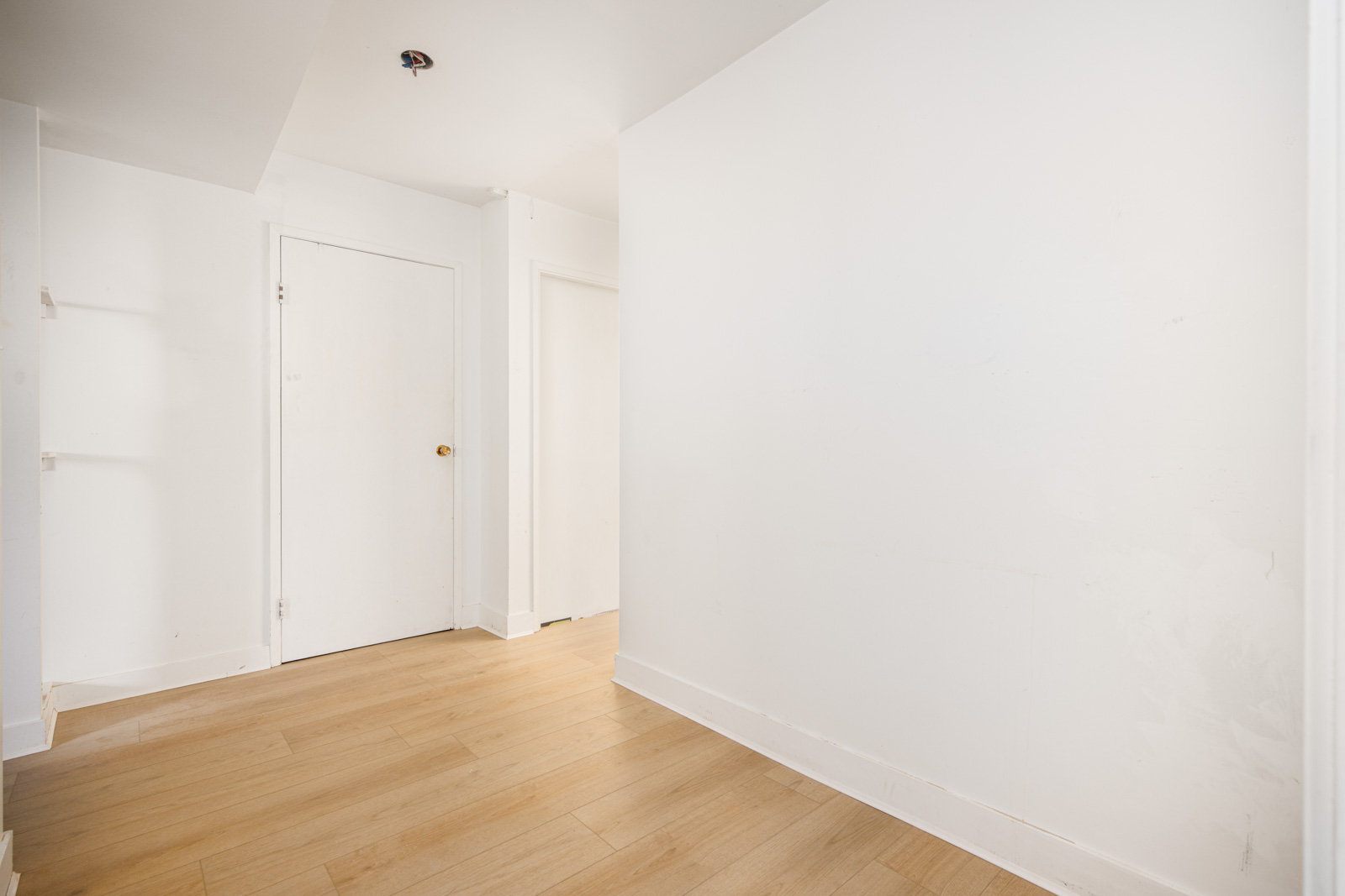 A bright, empty hallway with white walls, light wood flooring, and two closed white doors.
