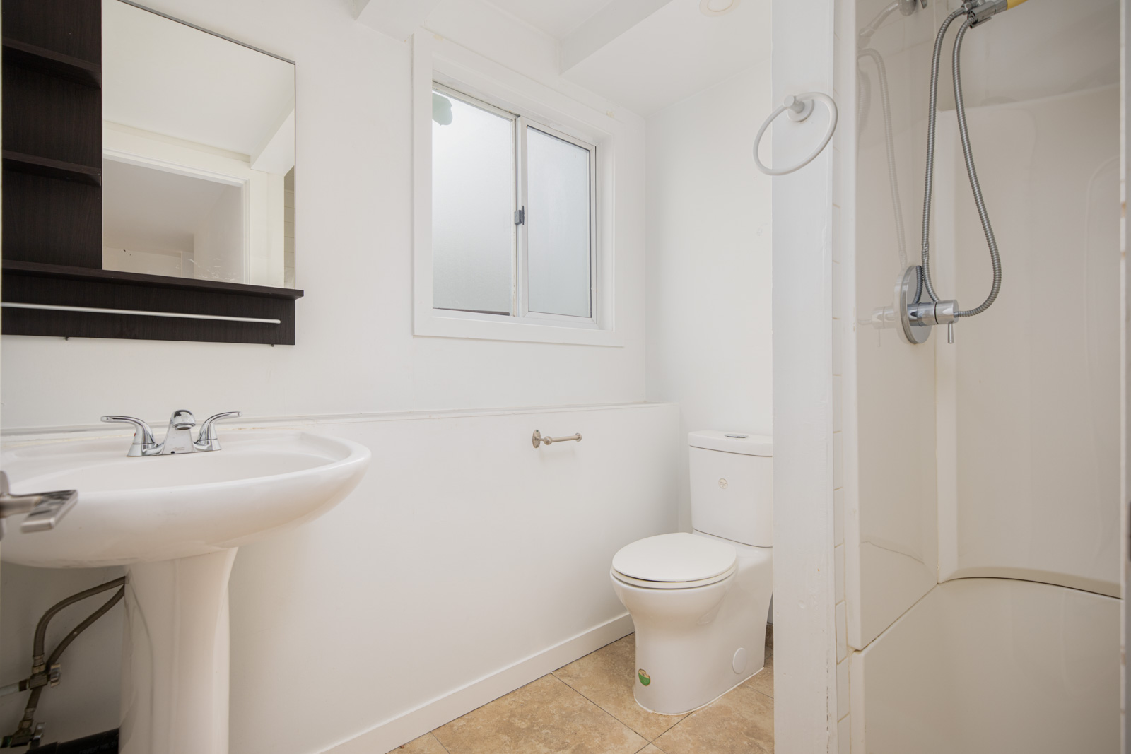 A small bathroom with a pedestal sink, wall mirror cabinet, toilet, frosted window, and a shower with a handheld showerhead.