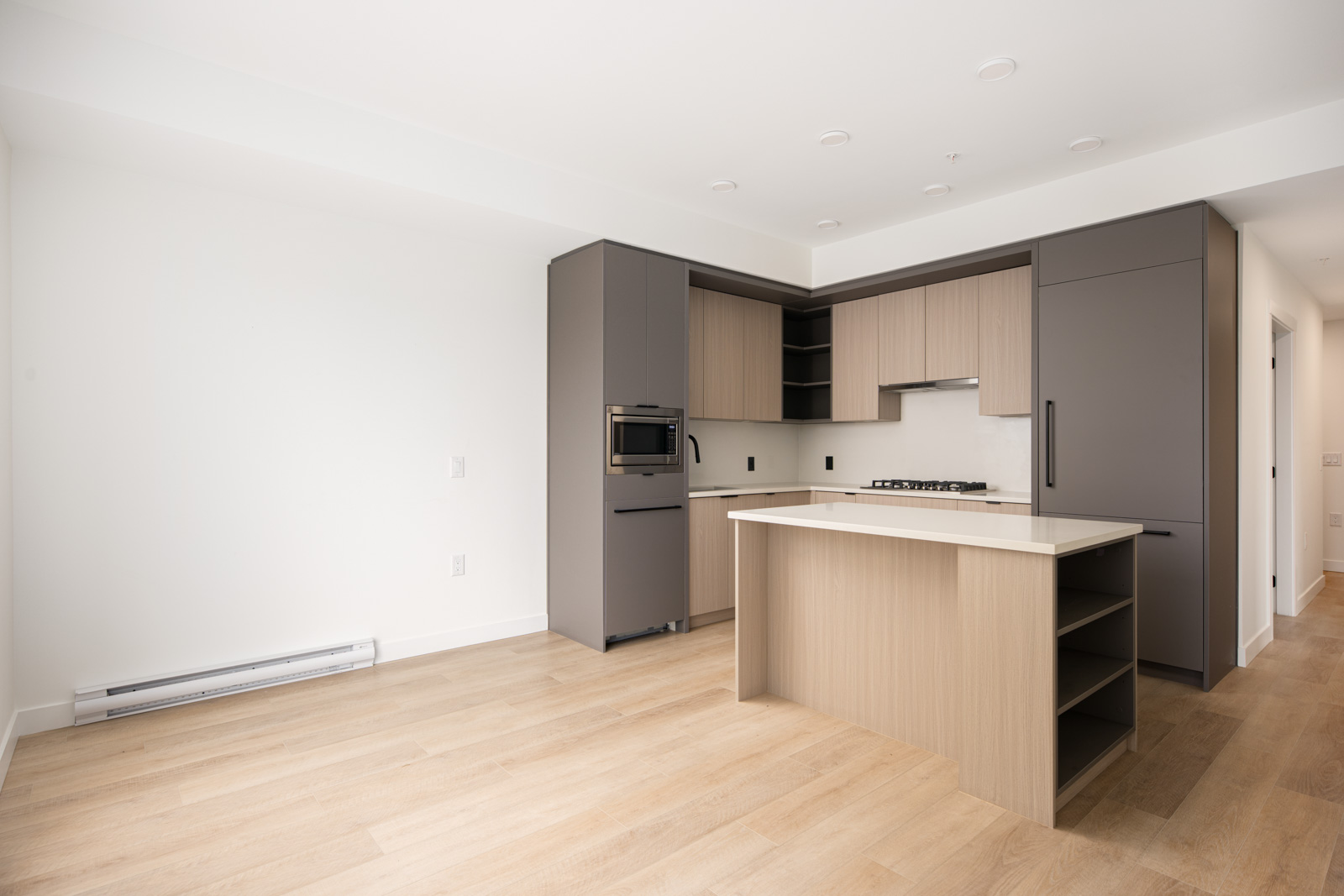 Modern kitchen with light wood floors, neutral cabinetry, built-in appliances, island with open shelves, and minimal decor in a bright, empty space.