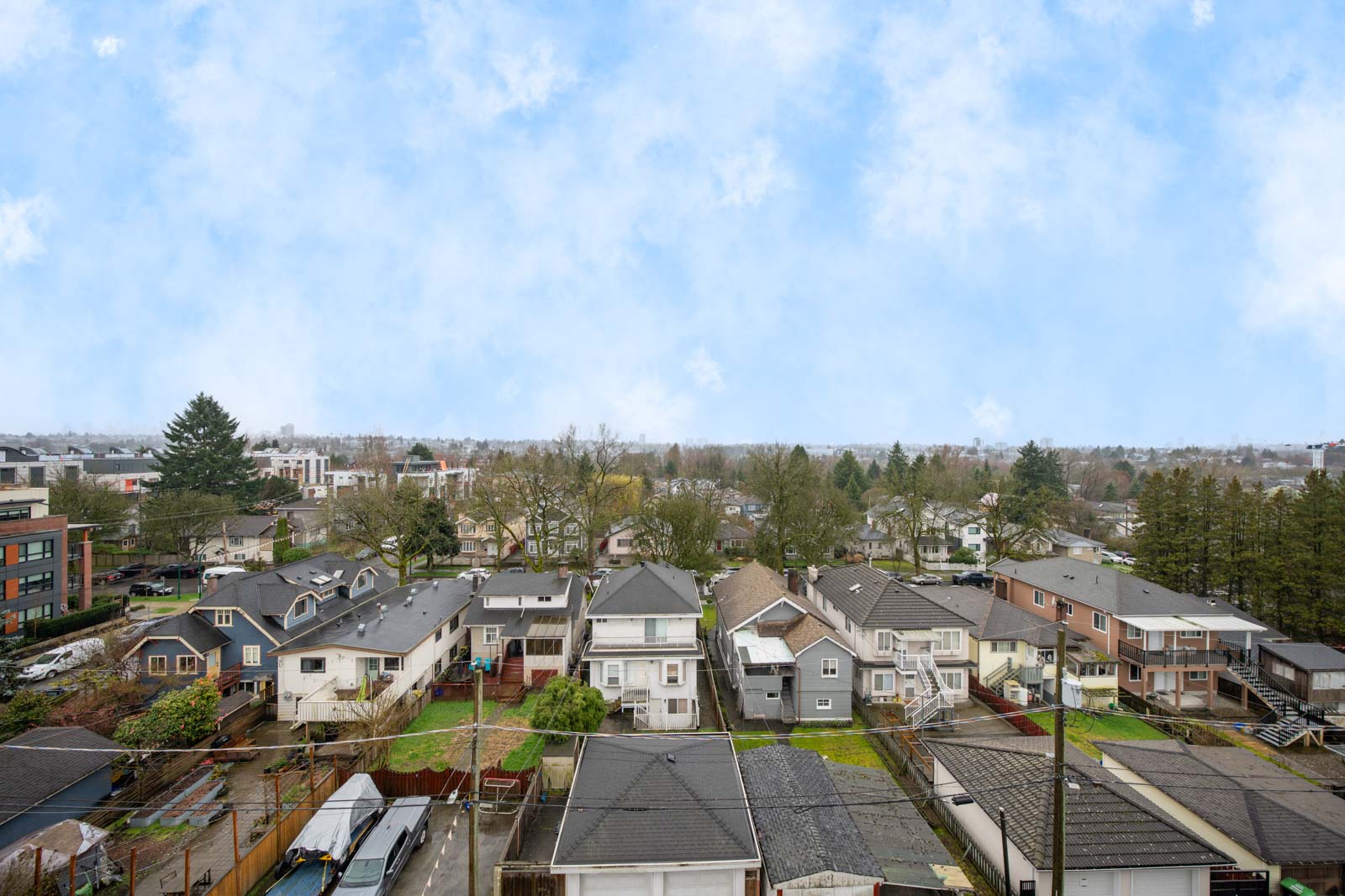 A daytime view of a suburban neighborhood with rows of houses, some trees, and a partly cloudy sky overhead.