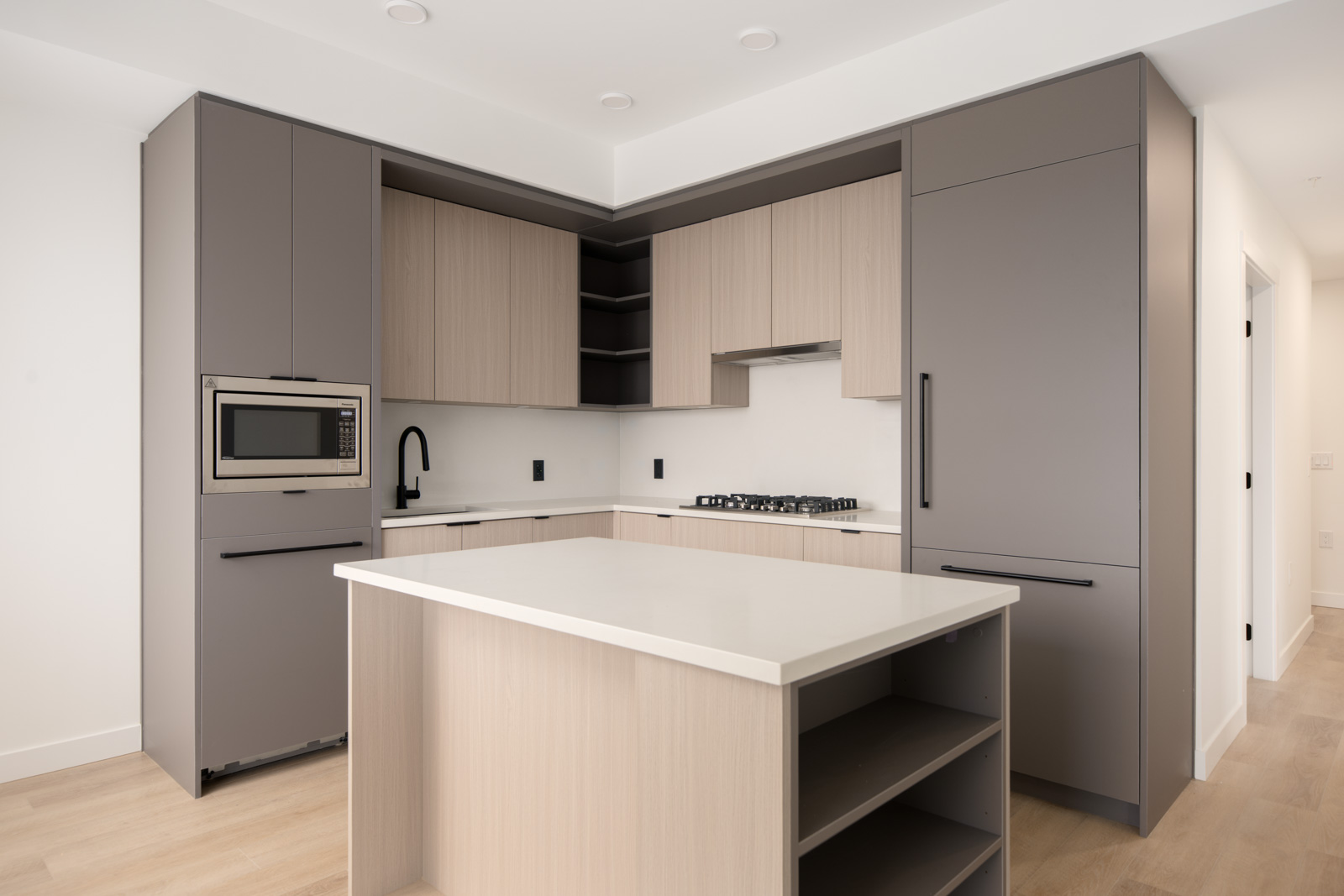 Modern kitchen with gray and light wood cabinets, a built-in microwave, gas stove, black fixtures, and a central island with open shelves.
