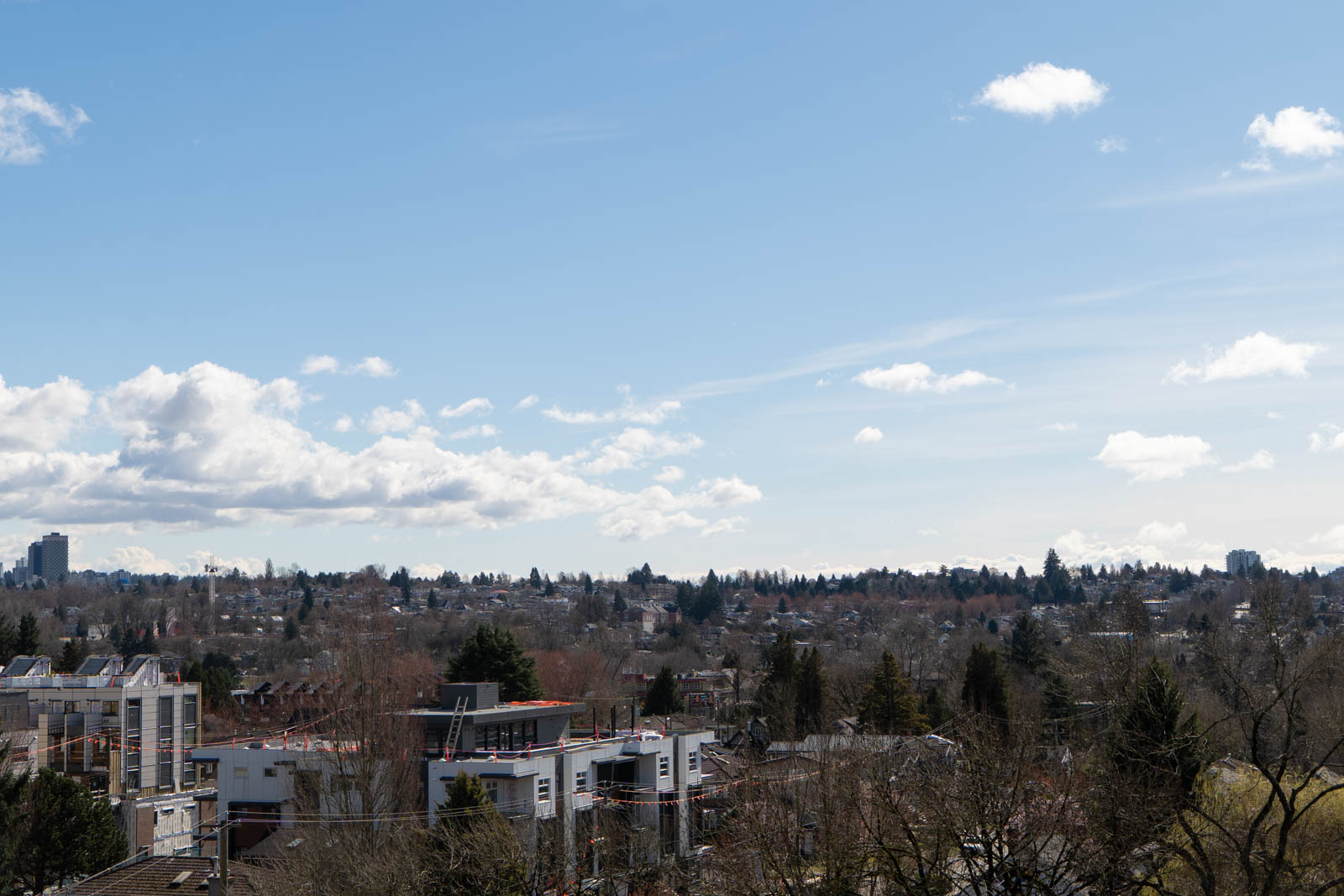 A cityscape with low-rise buildings, bare trees, and a clear blue sky with scattered clouds.
