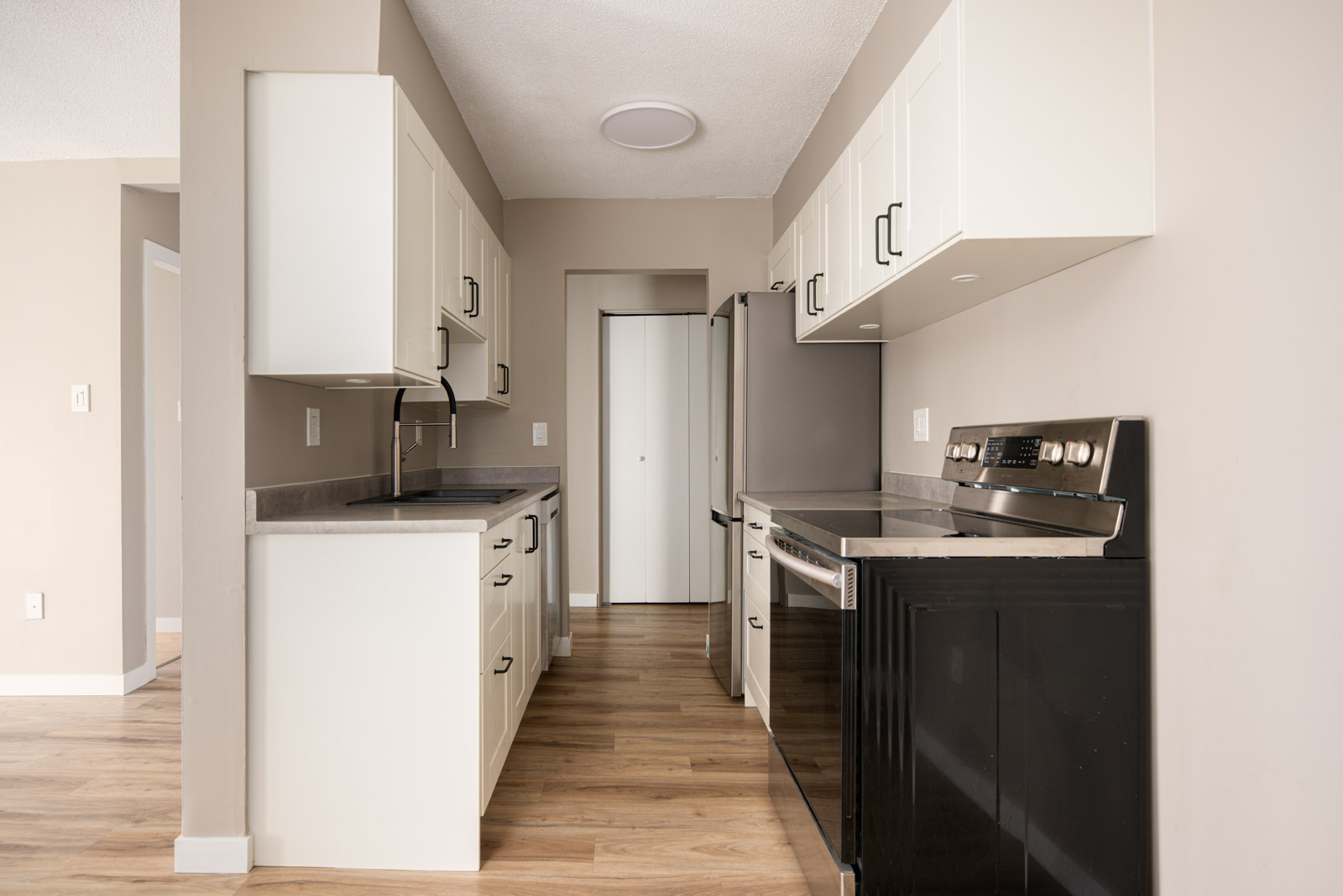Modern kitchen with white cabinets, stainless steel appliances, black countertops, and light wood flooring, viewed from the entrance.