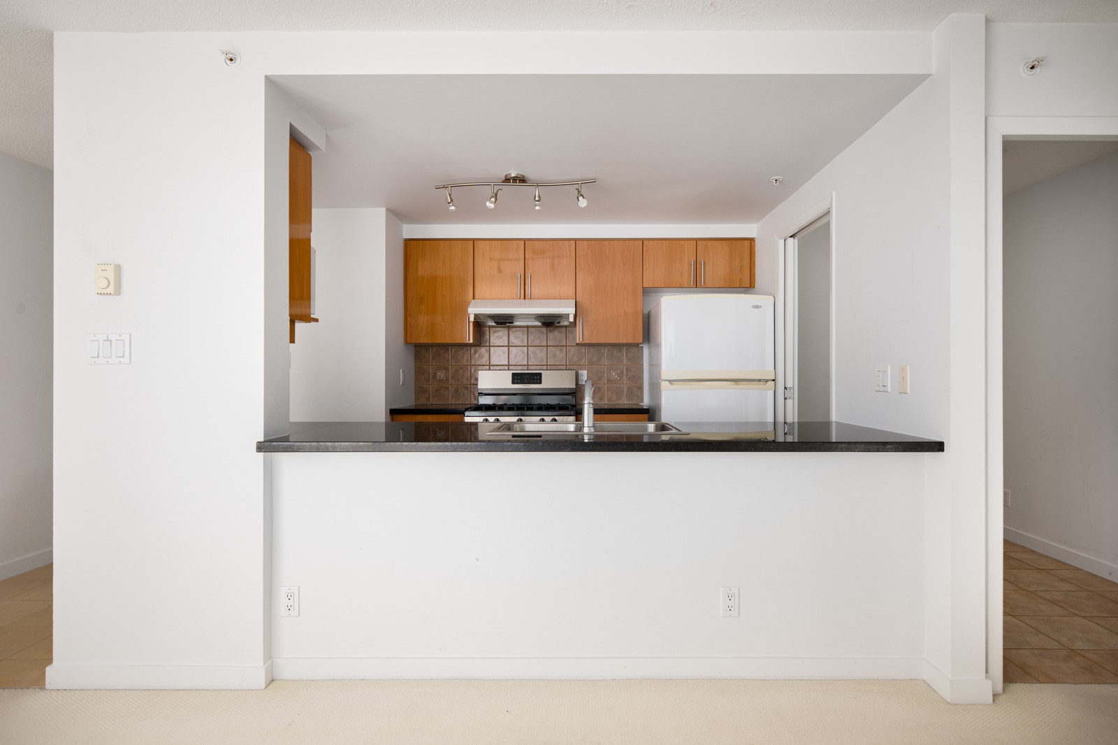 A modern kitchen with wooden cabinets, stainless steel appliances, a white fridge, a stove, and a black countertop with a sink and faucet.