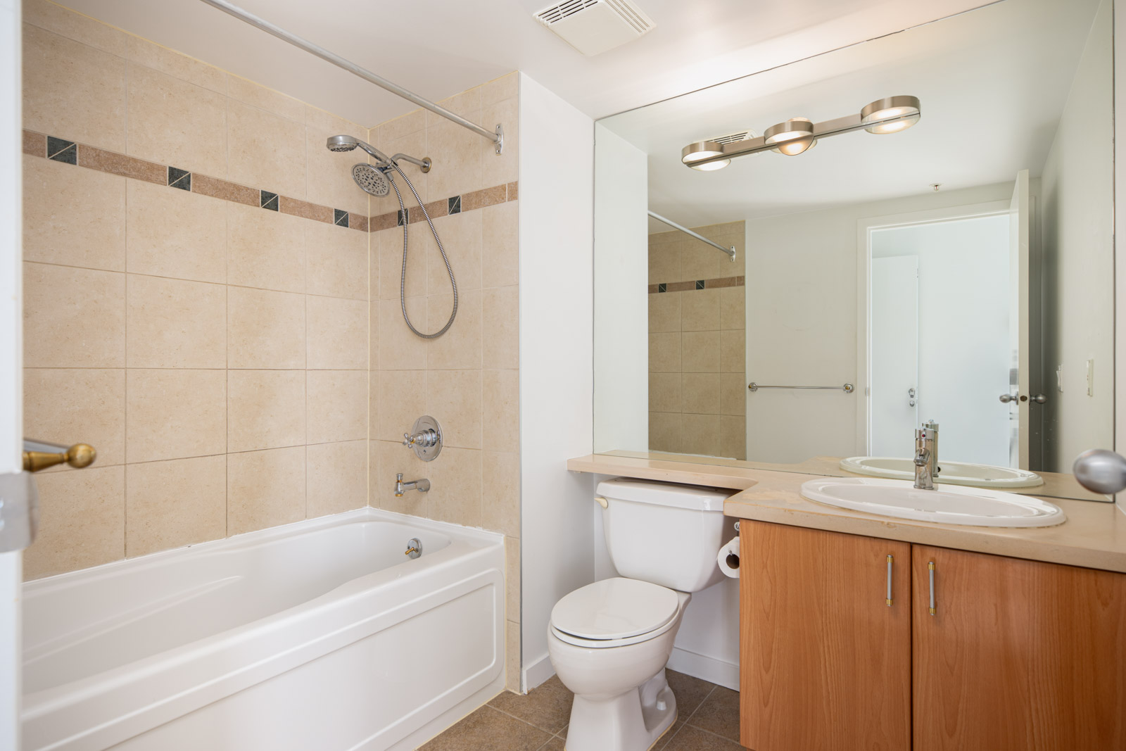 Modern bathroom with a bathtub-shower combo, single sink vanity, large mirror, and tan tile walls.