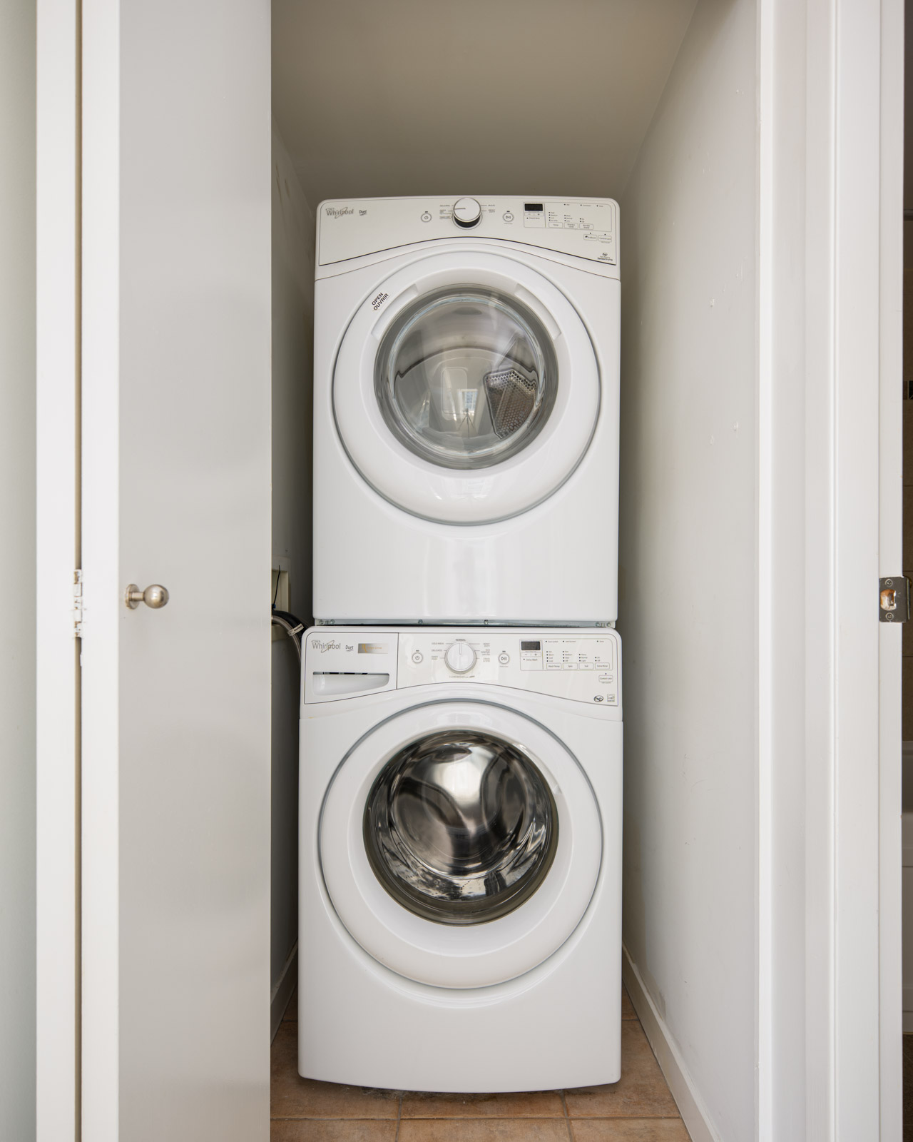A stacked white washer and dryer set is placed in a small laundry closet with the door partially open.