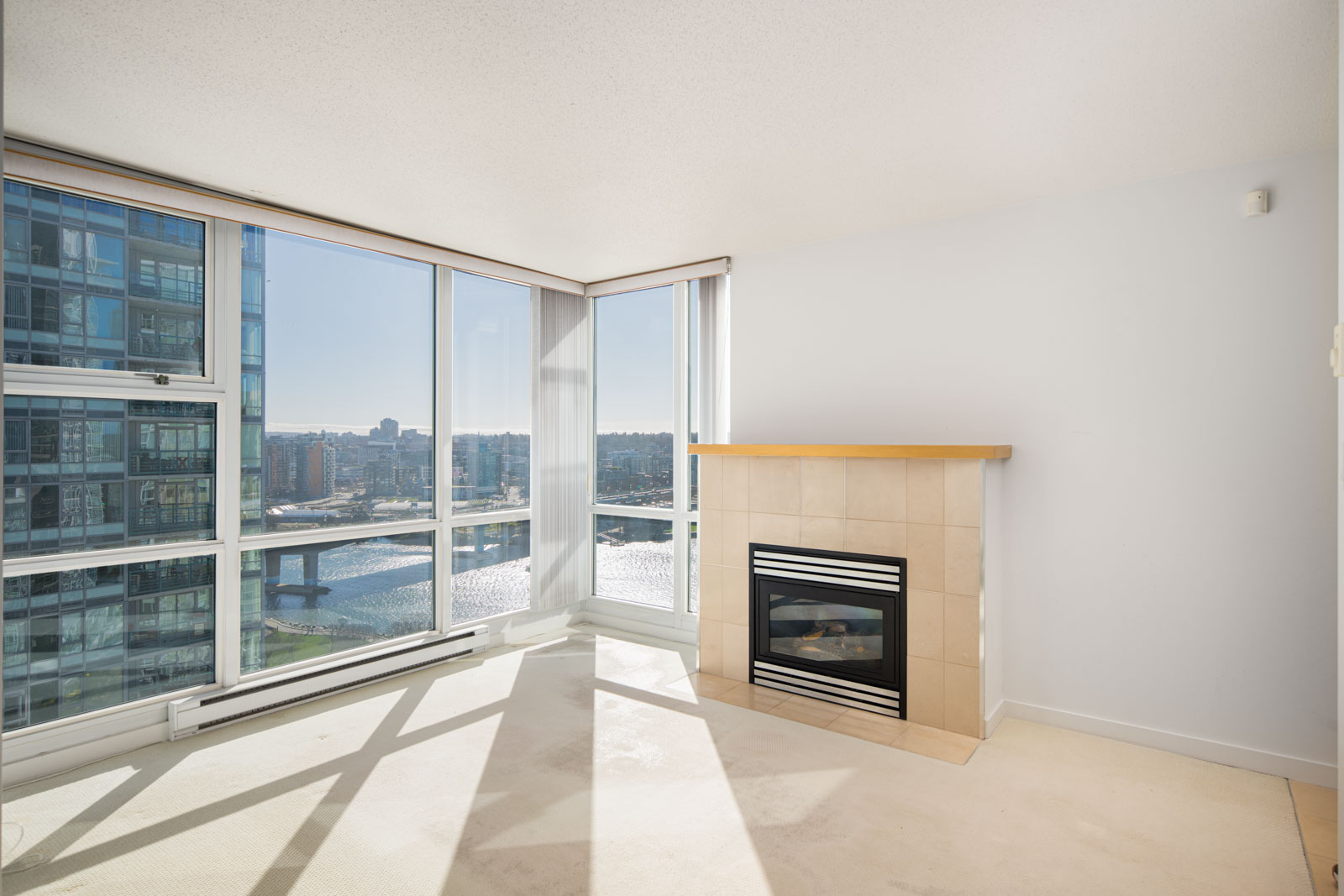 Corner room with large windows, city and water views, a gas fireplace with a tile surround, and neutral carpet flooring.