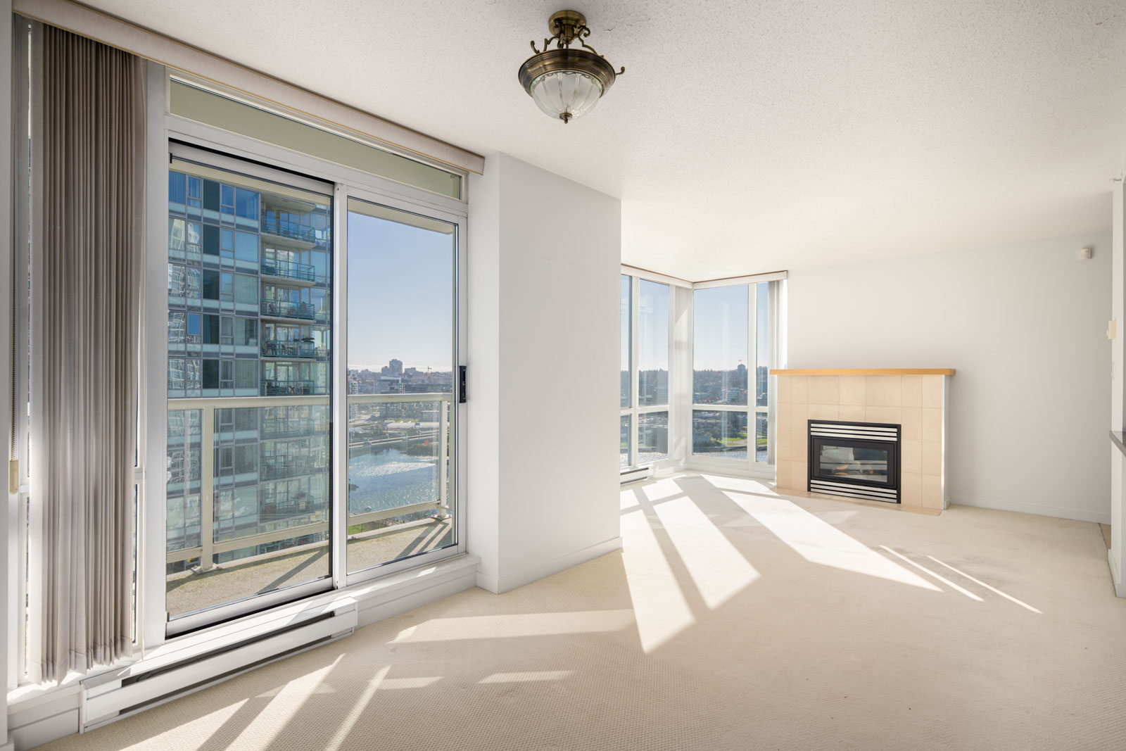 Bright living room with large windows, sliding glass door to a balcony, a fireplace, and a view of a modern building and water outside.
