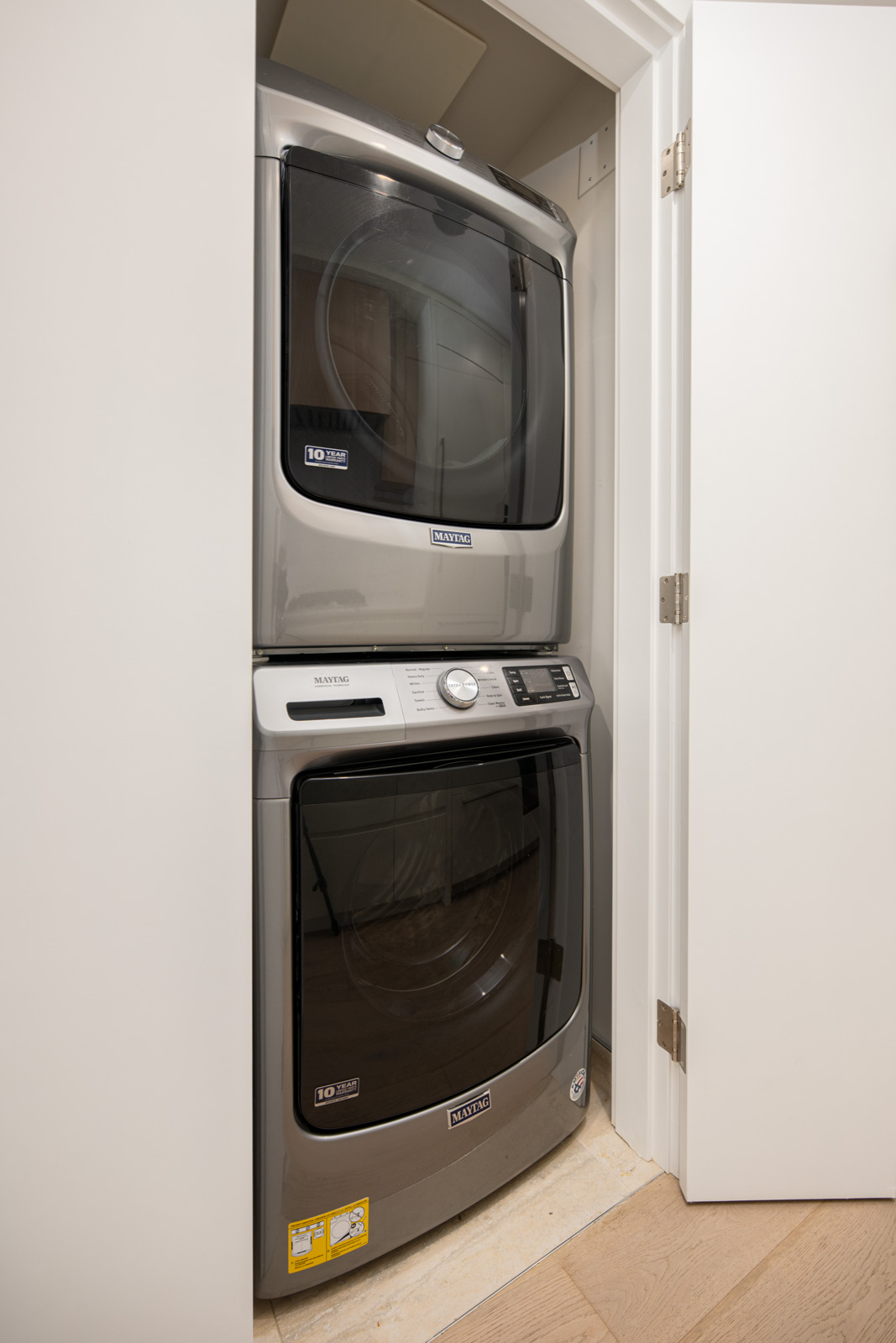 A stacked Samsung washer and dryer set is installed in a small laundry closet with white double doors.