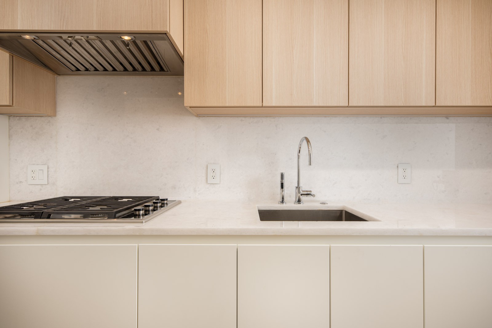 Modern kitchen with light wood cabinets, a built-in gas stove, marble backsplash, stainless steel faucet, and a rectangular sink.