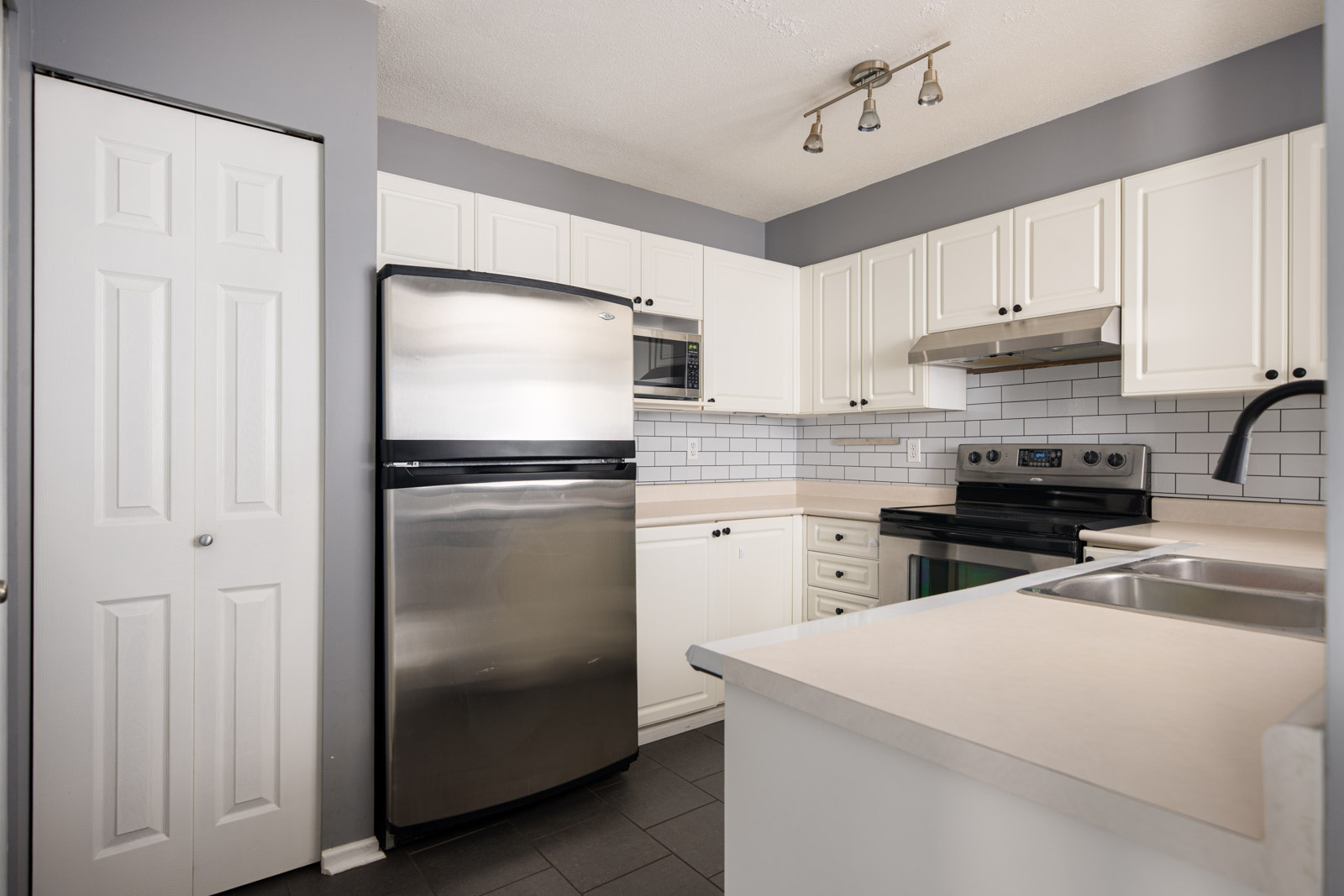 Modern kitchen with white cabinets, stainless steel appliances, subway tile backsplash, gray walls, and black tile flooring.