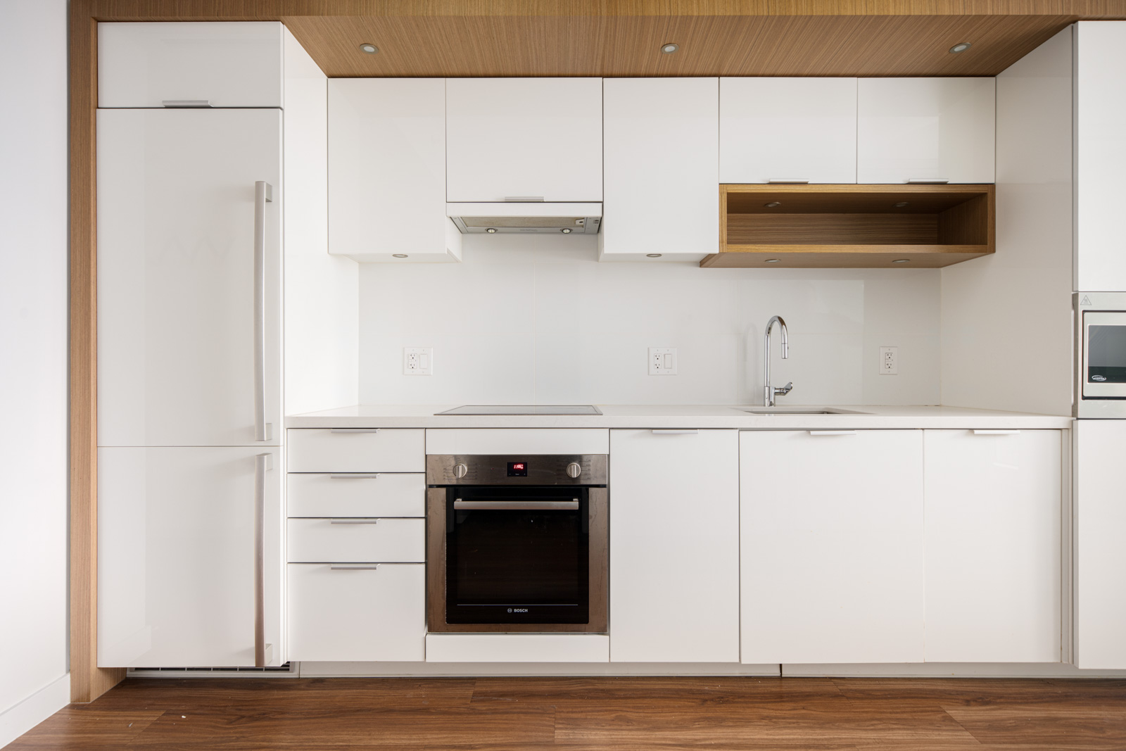 Modern kitchen with white cabinets, built-in appliances, electric stove, oven, refrigerator, and a sink, featuring wood accents and a clean, minimalist design.