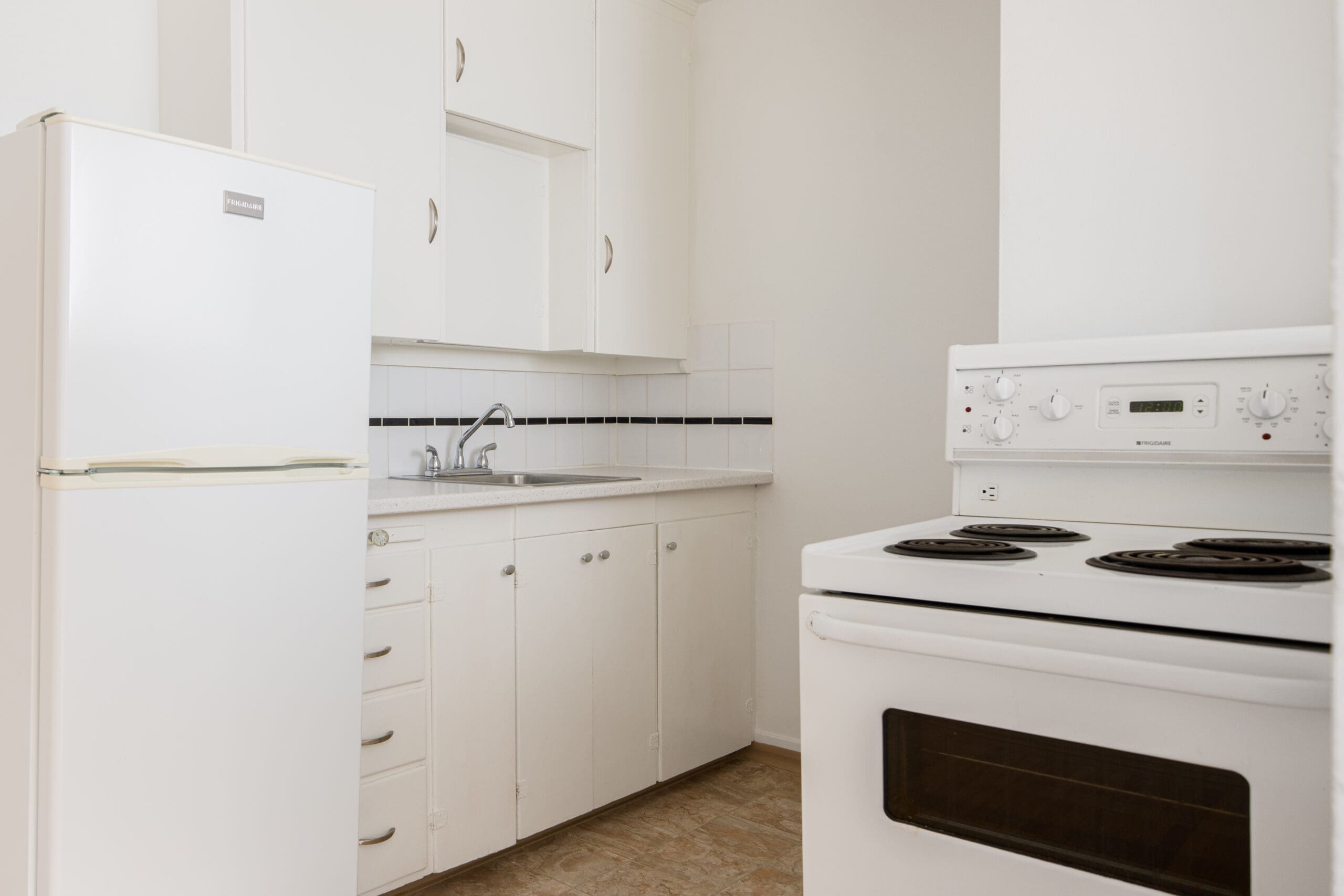 A small kitchen with white cabinets, a white refrigerator, a stainless steel sink, and a white electric stove with four burners.