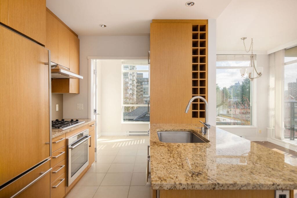 Modern kitchen with light wood cabinets, granite countertops, a built-in oven, gas stovetop, wine rack, and large windows letting in natural light.