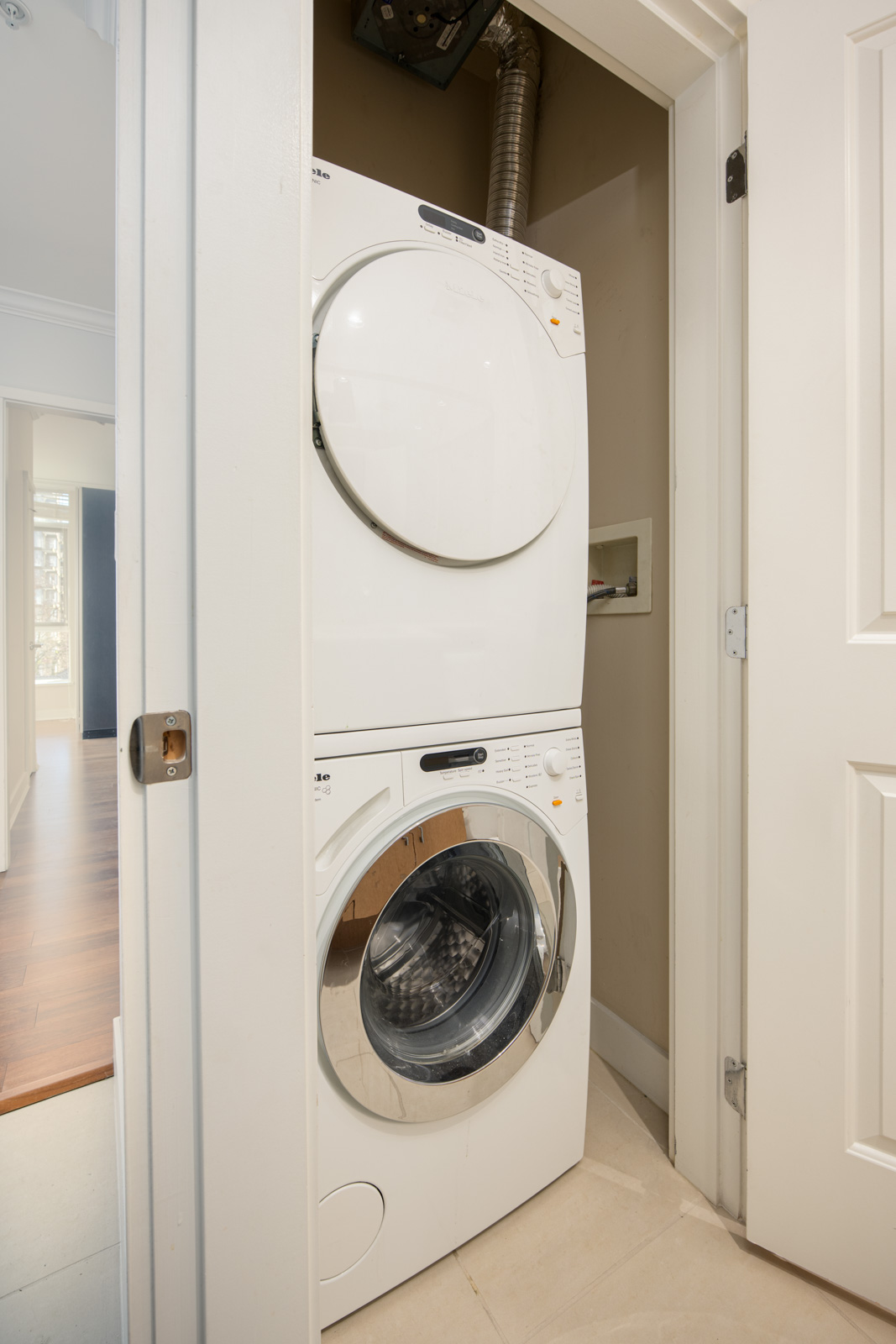 A stacked washer and dryer unit is installed in a small laundry closet with the dryer on top and the washing machine door open.