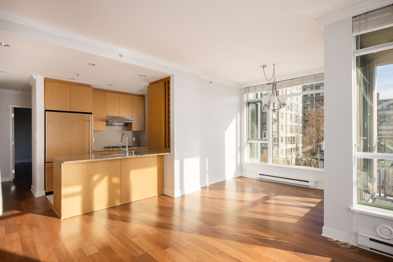 Bright, unfurnished apartment with wood floors, open kitchen with light wood cabinets, granite countertop, large windows, and city views.