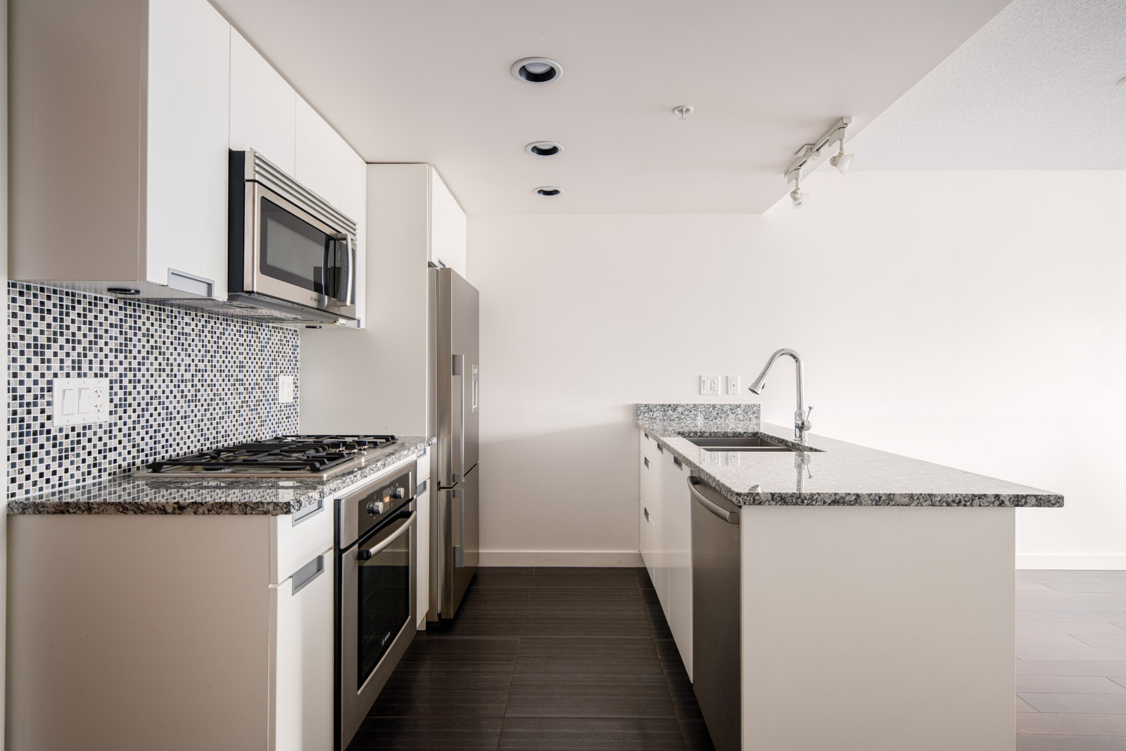Modern kitchen with white cabinets, stainless steel appliances, mosaic tile backsplash, and a granite countertop island with a sink.