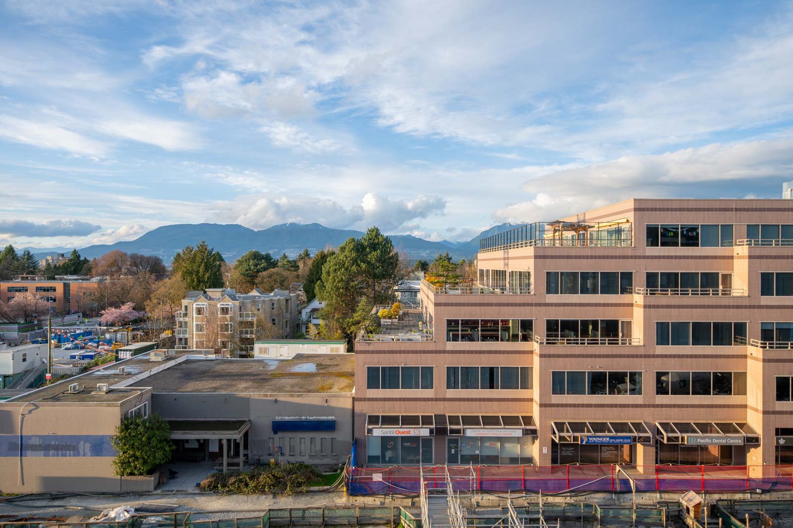 Office and residential buildings with trees and mountains in the background under a partly cloudy sky.