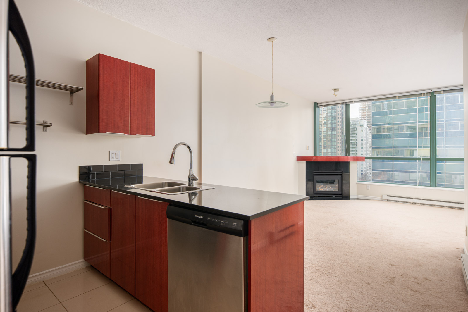 Modern apartment interior with a kitchen featuring red cabinets, stainless steel appliances, and an open living area with large windows and a fireplace.