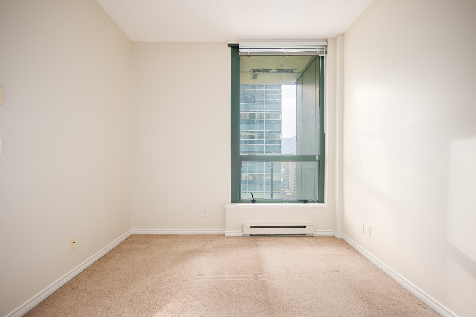 Empty room with beige carpet, off-white walls, and a large window showing a cityscape outside.