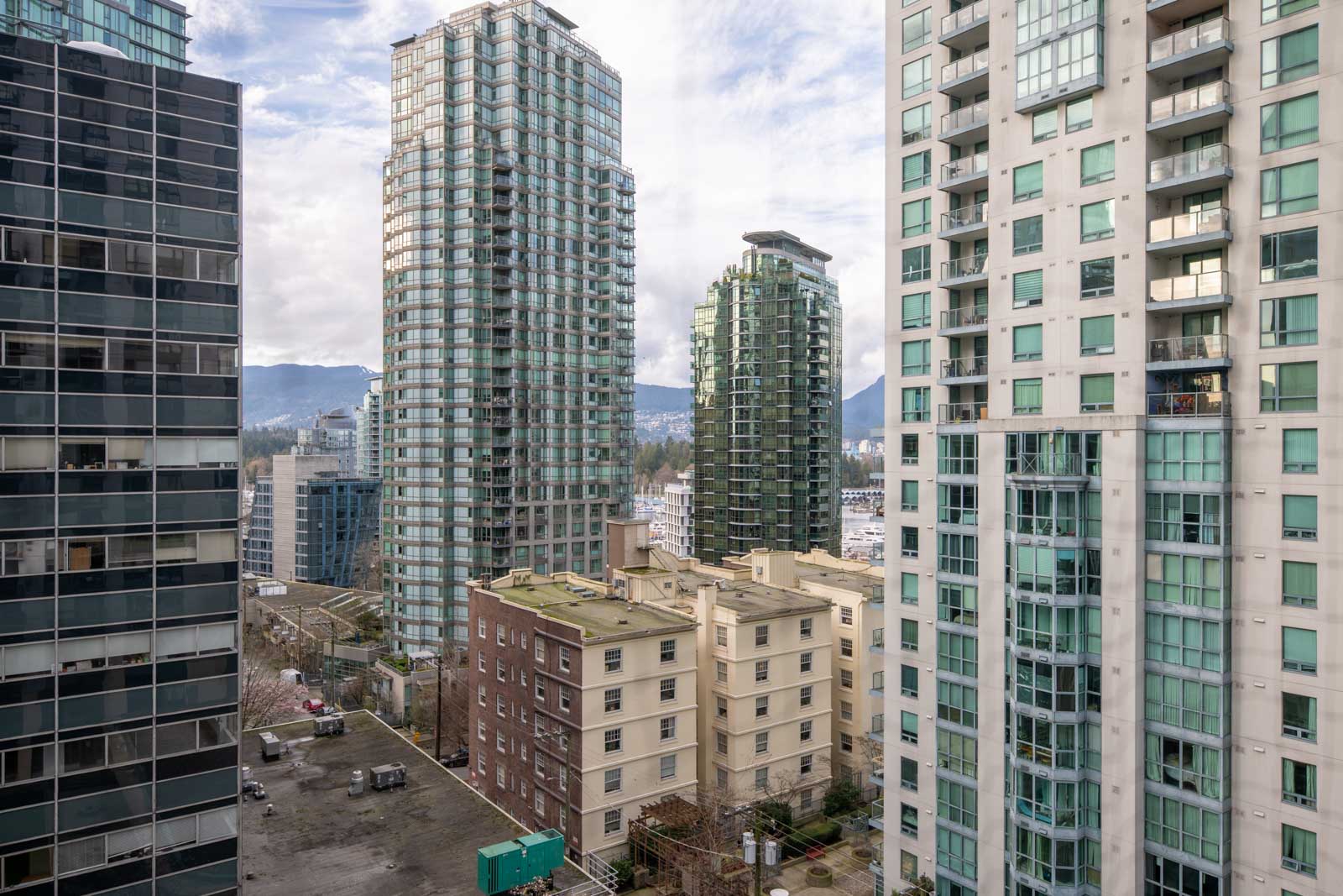 High-rise residential buildings surround older mid-rise apartments, with mountains visible in the background under a partly cloudy sky.