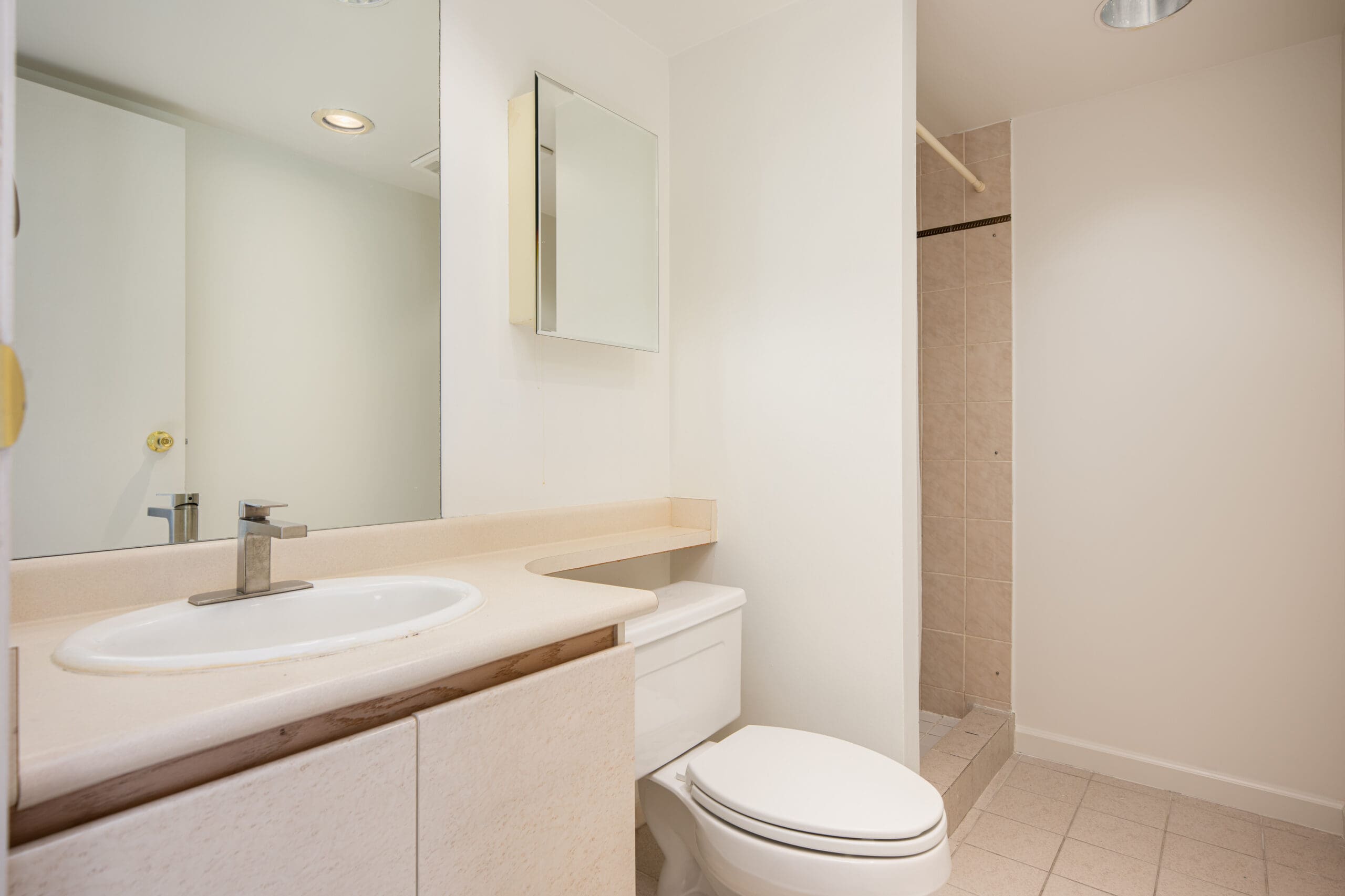 A modern bathroom with a white sink, countertop, and toilet, a wall-mounted mirror cabinet, and a walk-in shower with beige tiles.