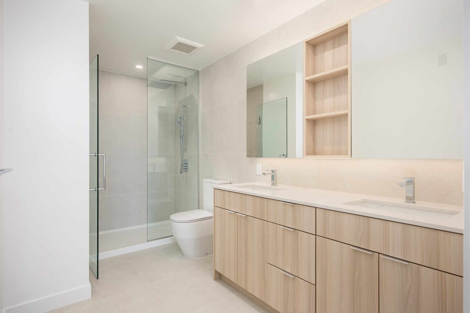 Modern bathroom with light wood double-sink vanity, large mirror, open shelves, glass-enclosed shower, and neutral tiled walls and floor.