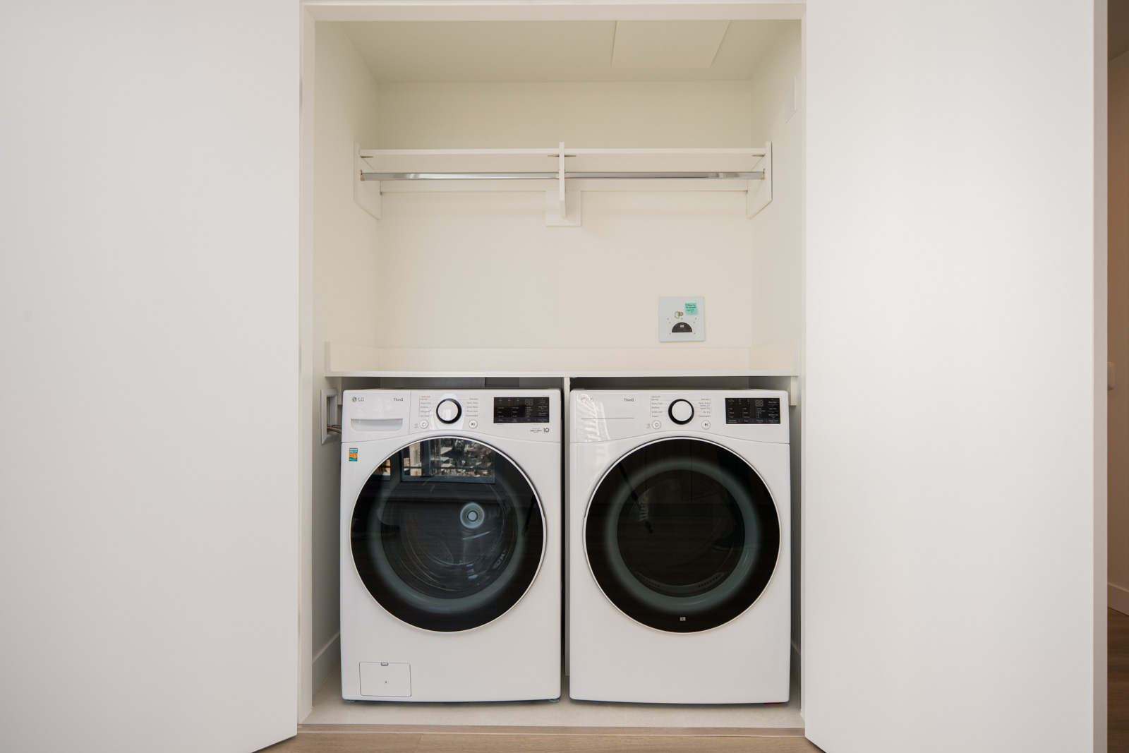 A front-loading washing machine and dryer are placed side by side in a recessed laundry nook with a shelf and hanging rod above them.