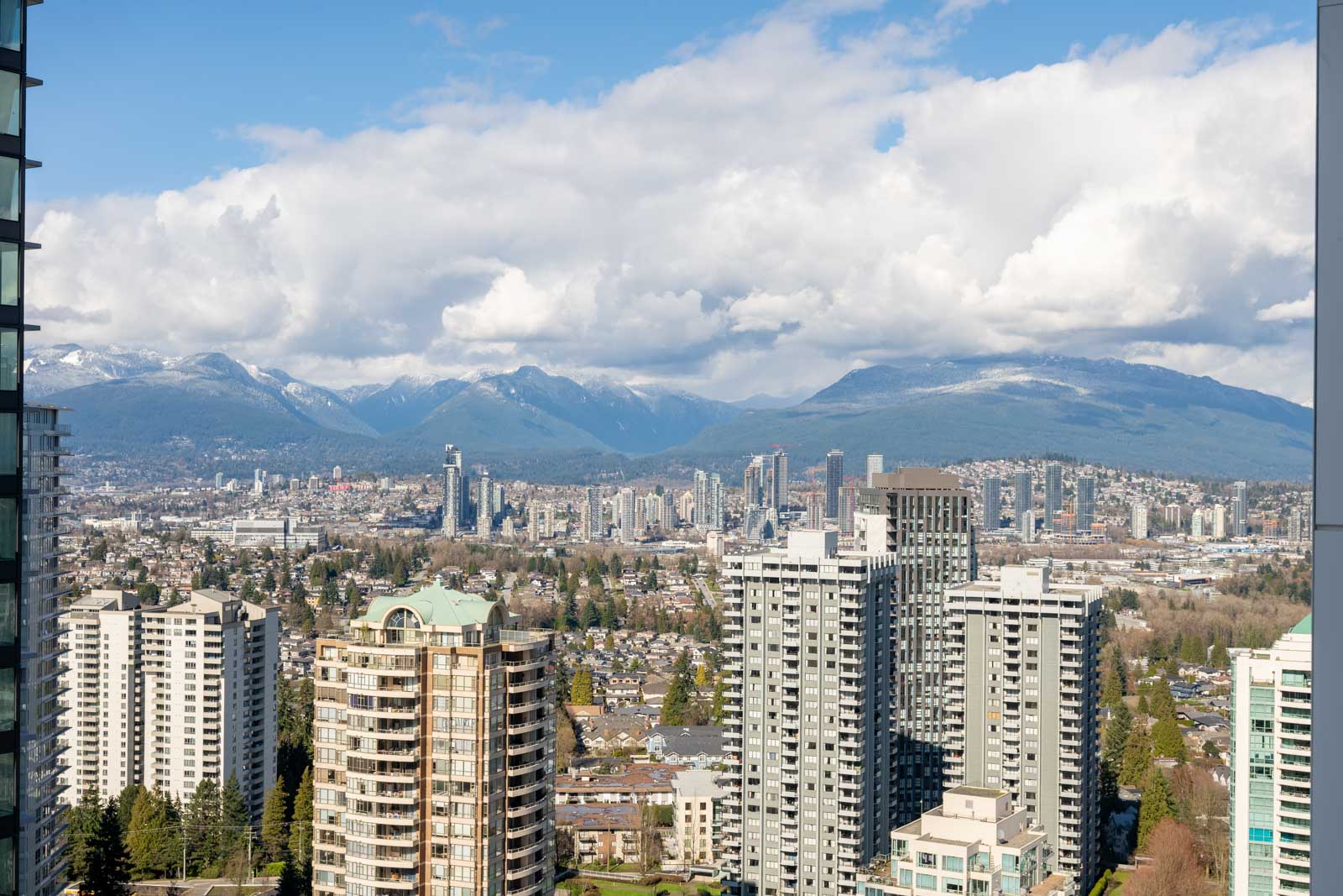 High-rise buildings in the foreground with a cityscape and mountains in the background under a partly cloudy sky.