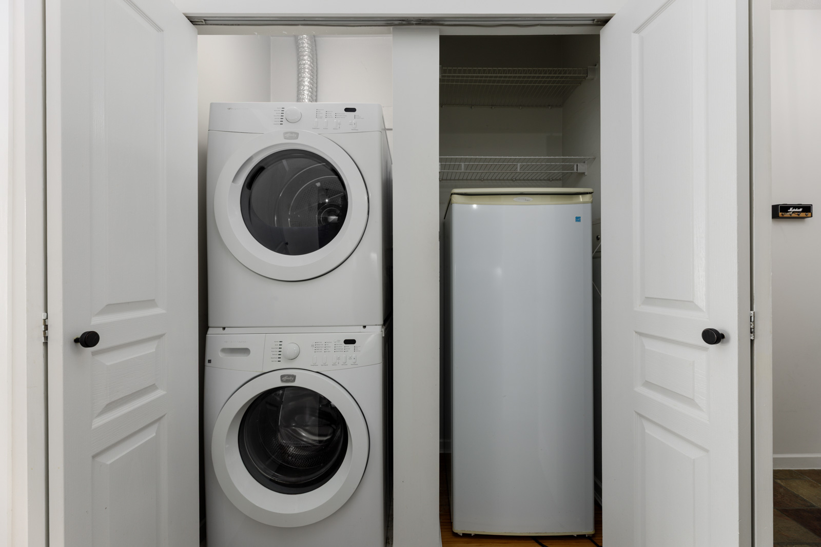 Stacked washer and dryer next to a white refrigerator inside a closet with double doors open.