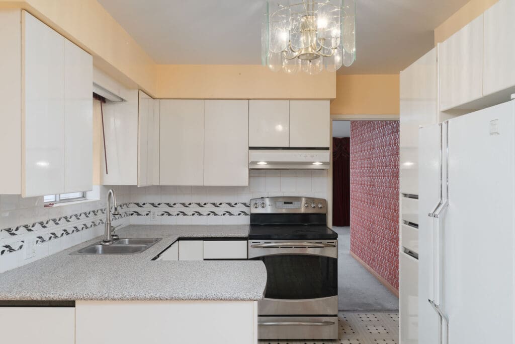A modern kitchen with white cabinets, stainless steel appliances, a patterned backsplash, and a granite countertop under a glass chandelier.