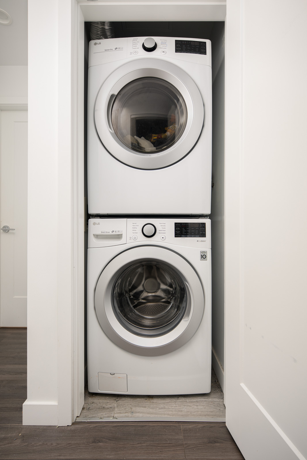 A stacked washer and dryer set in a small laundry closet with white walls and a dark wood floor.
