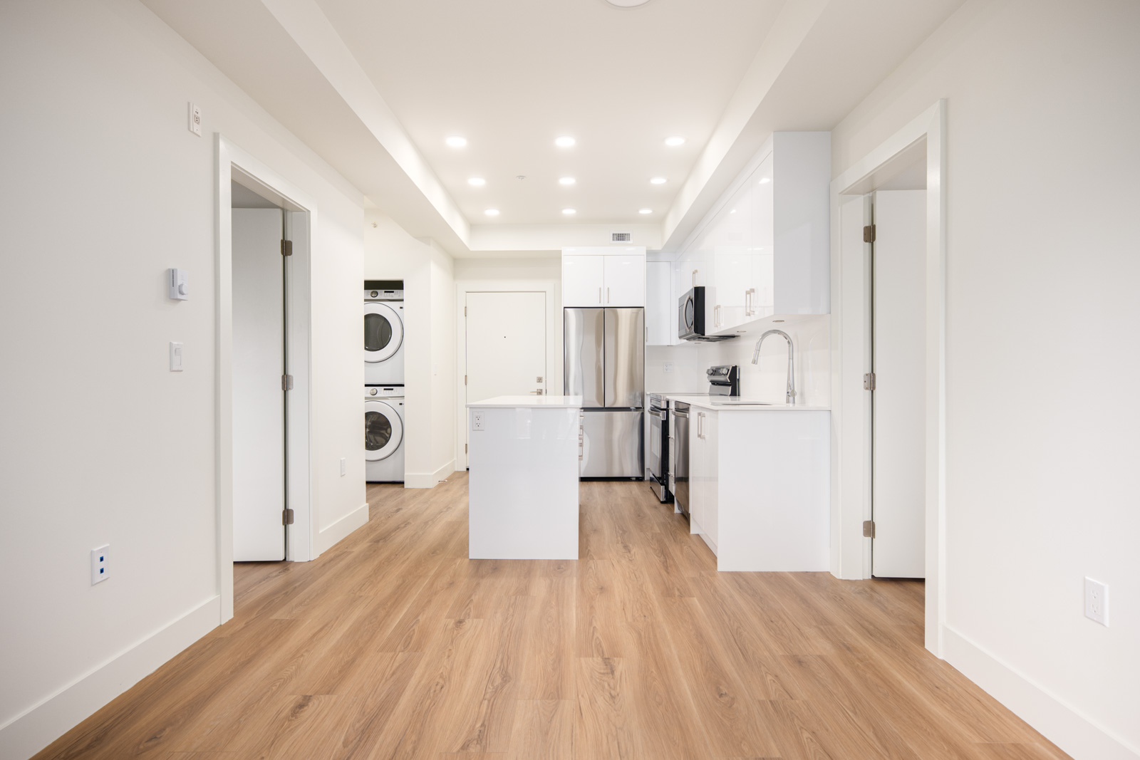 Modern kitchen with white cabinets, stainless steel appliances, center island, wood flooring, and a stacked washer and dryer visible in an adjacent alcove.