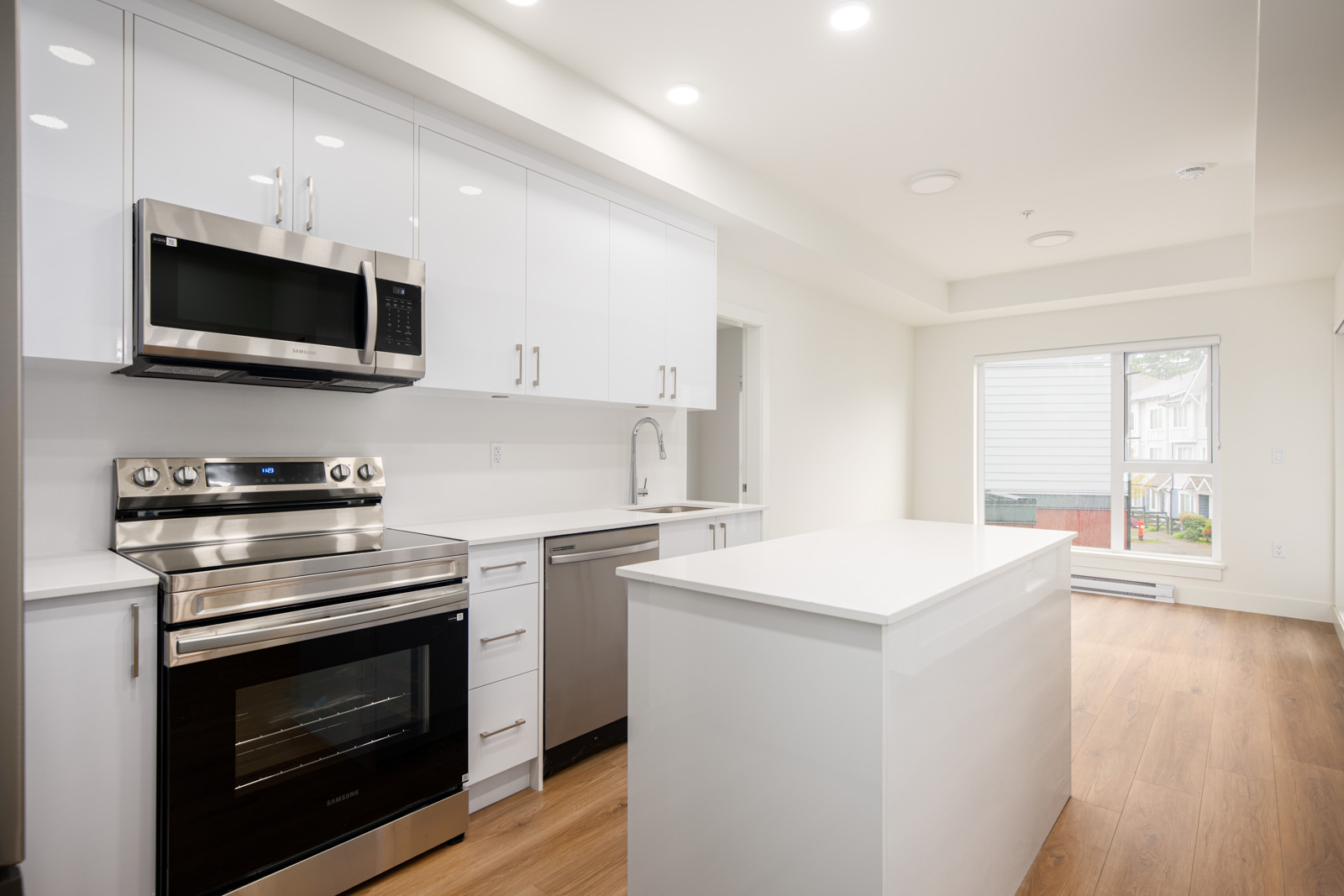 Modern kitchen with white cabinets, stainless steel appliances, a central island, wood flooring, and large window letting in natural light.