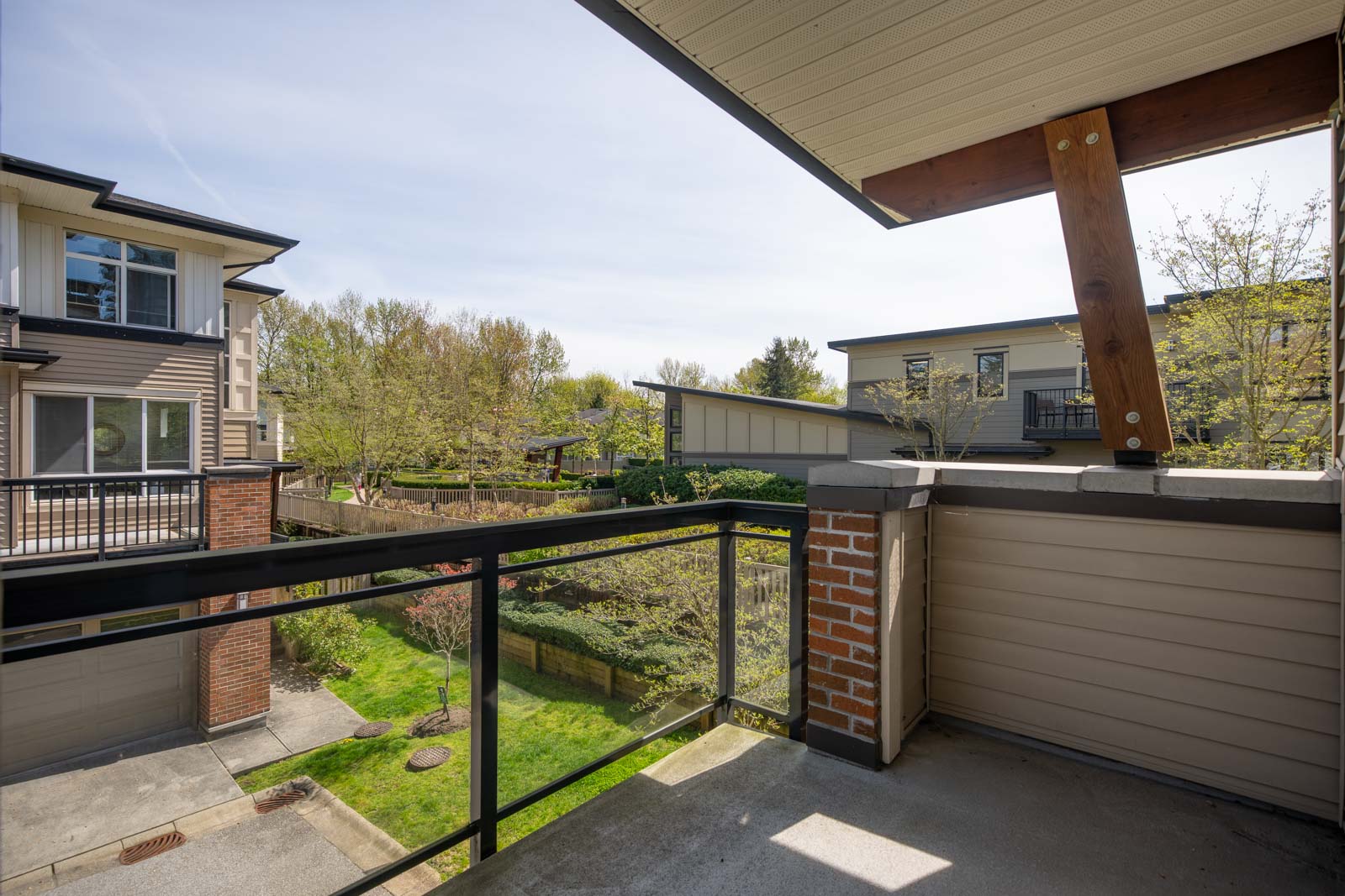 View from a balcony overlooking a residential area with modern houses, greenery, and a clear sky.