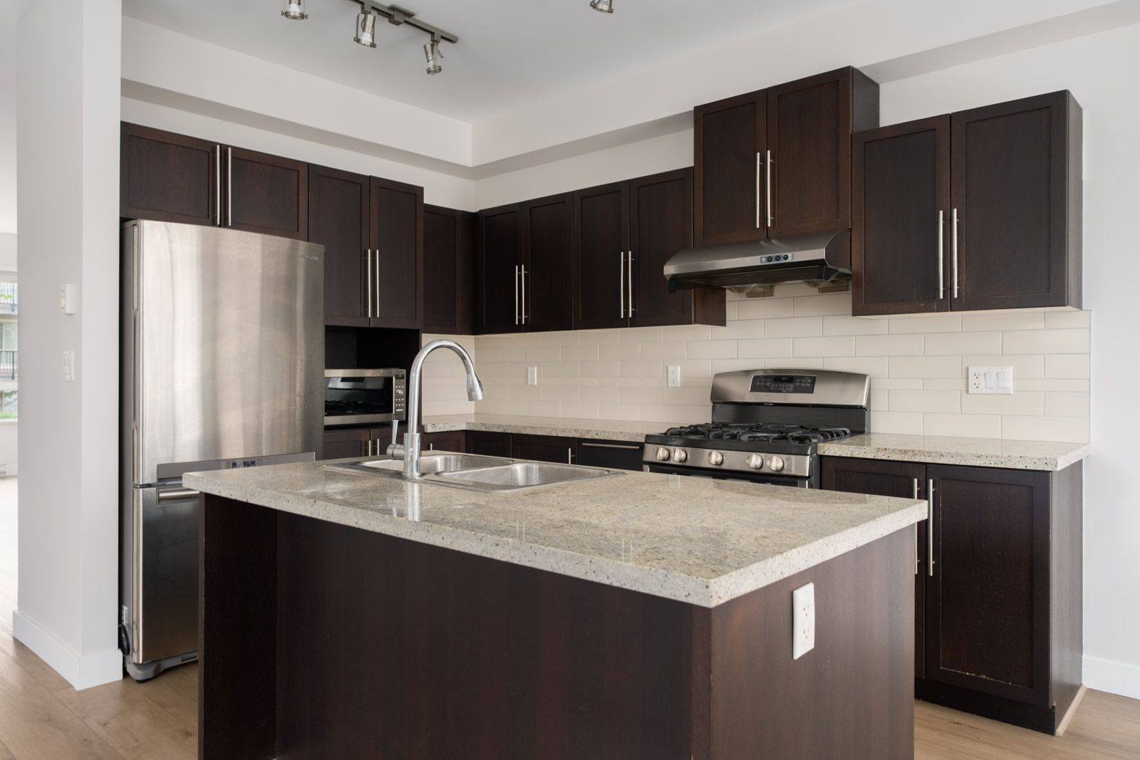 Modern kitchen with dark wood cabinets, stainless steel appliances, a large island with a sink, and a tiled backsplash.