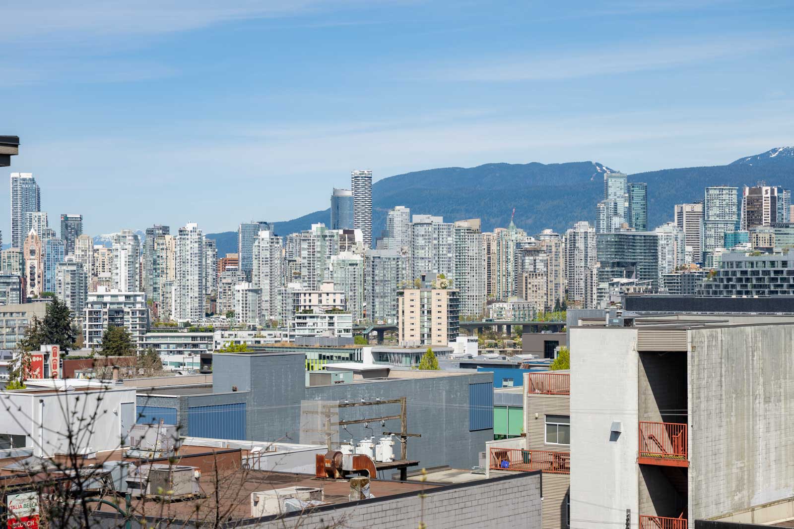A cityscape with modern high-rise buildings under a clear sky, mountains visible in the background, and low-rise structures in the foreground.