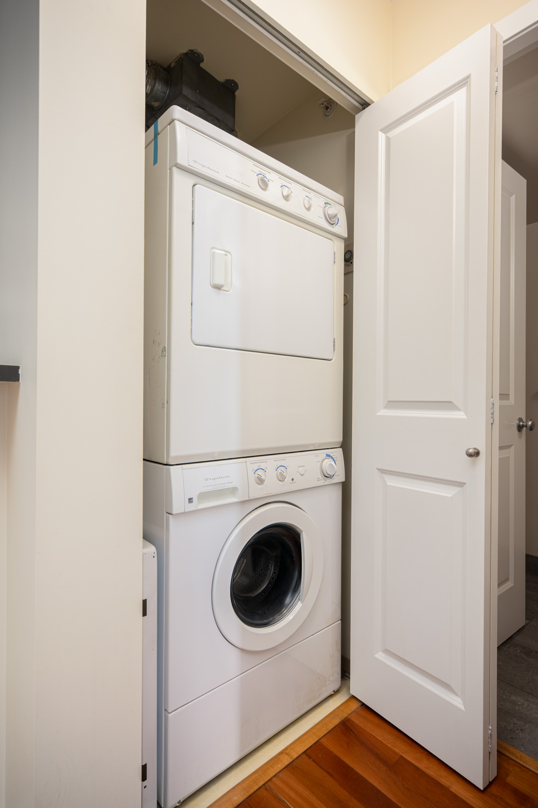 A stacked washer and dryer unit is installed in a small closet with open white doors, revealing the laundry appliances.
