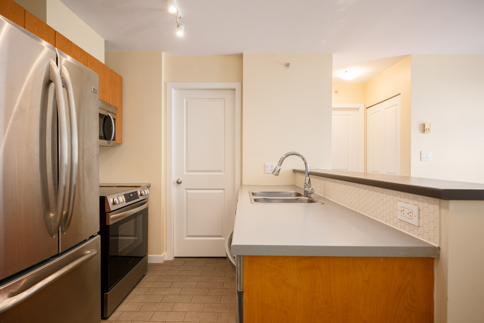 Modern kitchen with stainless steel appliances, a built-in oven, microwave, double sink, and light-colored cabinets and countertops.