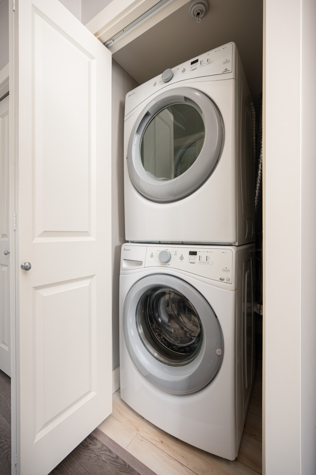 A stacked washer and dryer set is placed inside a small closet with white double doors on either side.
