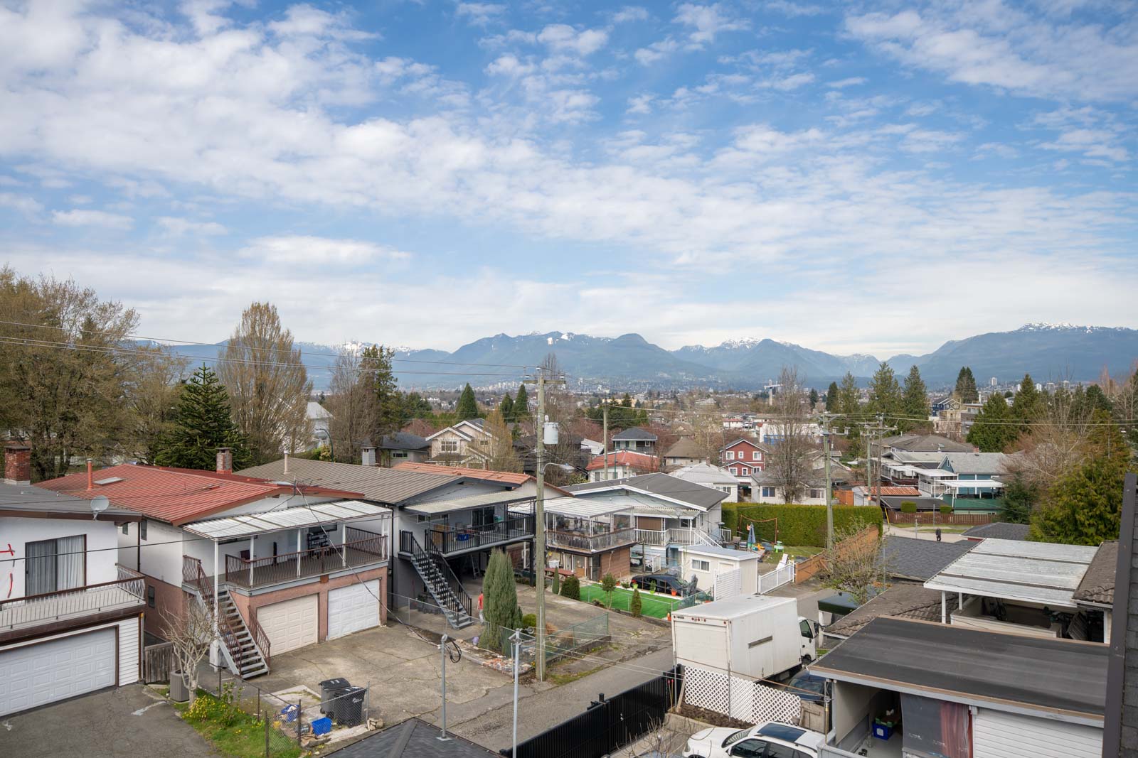 Residential neighborhood with houses, garages, and yards in the foreground, mountains in the distance, and a partly cloudy sky overhead.