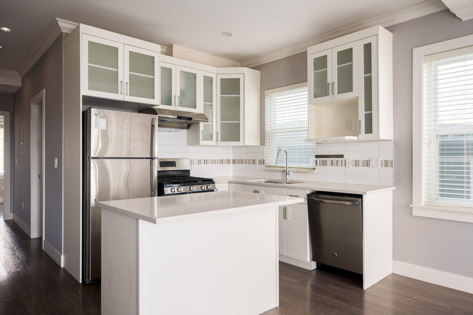 Modern kitchen with white cabinets, stainless steel appliances, a small island, and windows letting in natural light.