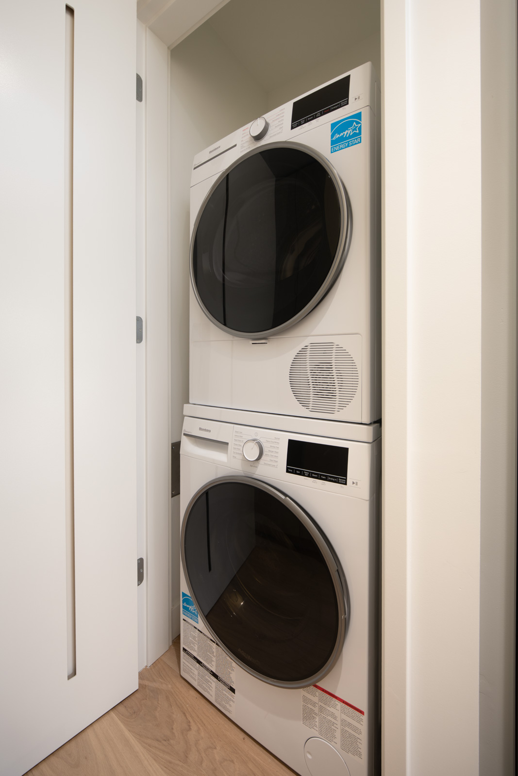 A stacked washer and dryer set is placed in a narrow laundry closet with a sliding white door.