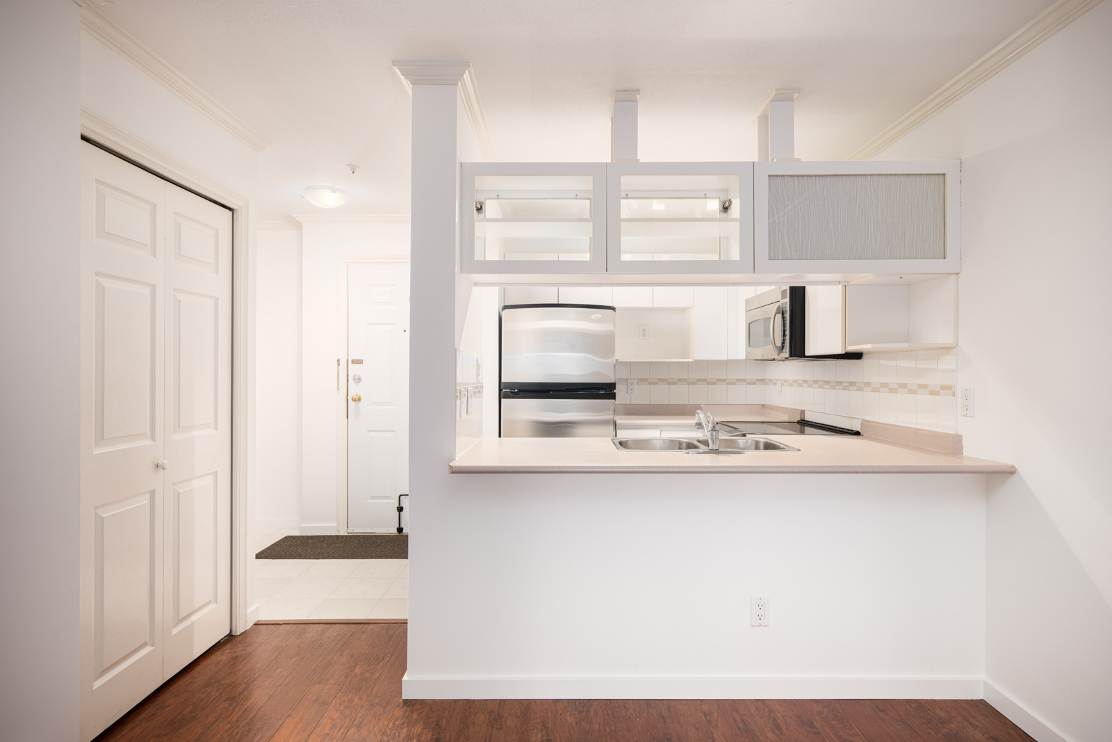 A modern kitchen with stainless steel appliances, white cabinets, a double sink, and an open counter facing the entrance of the home.